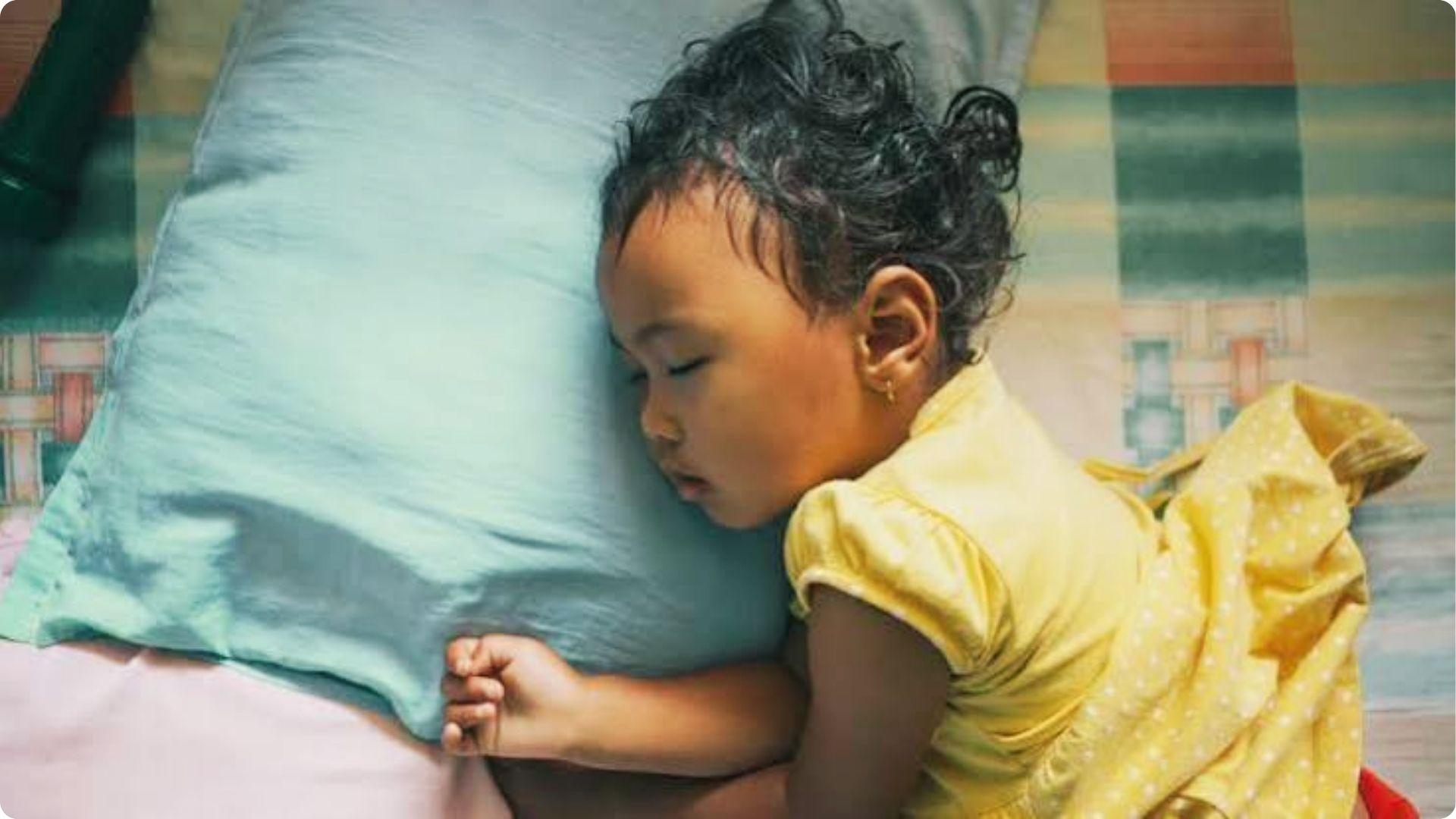 Toddler in yellow dress sleeping on pillow, showing how babies sweat to regulate body heat.
