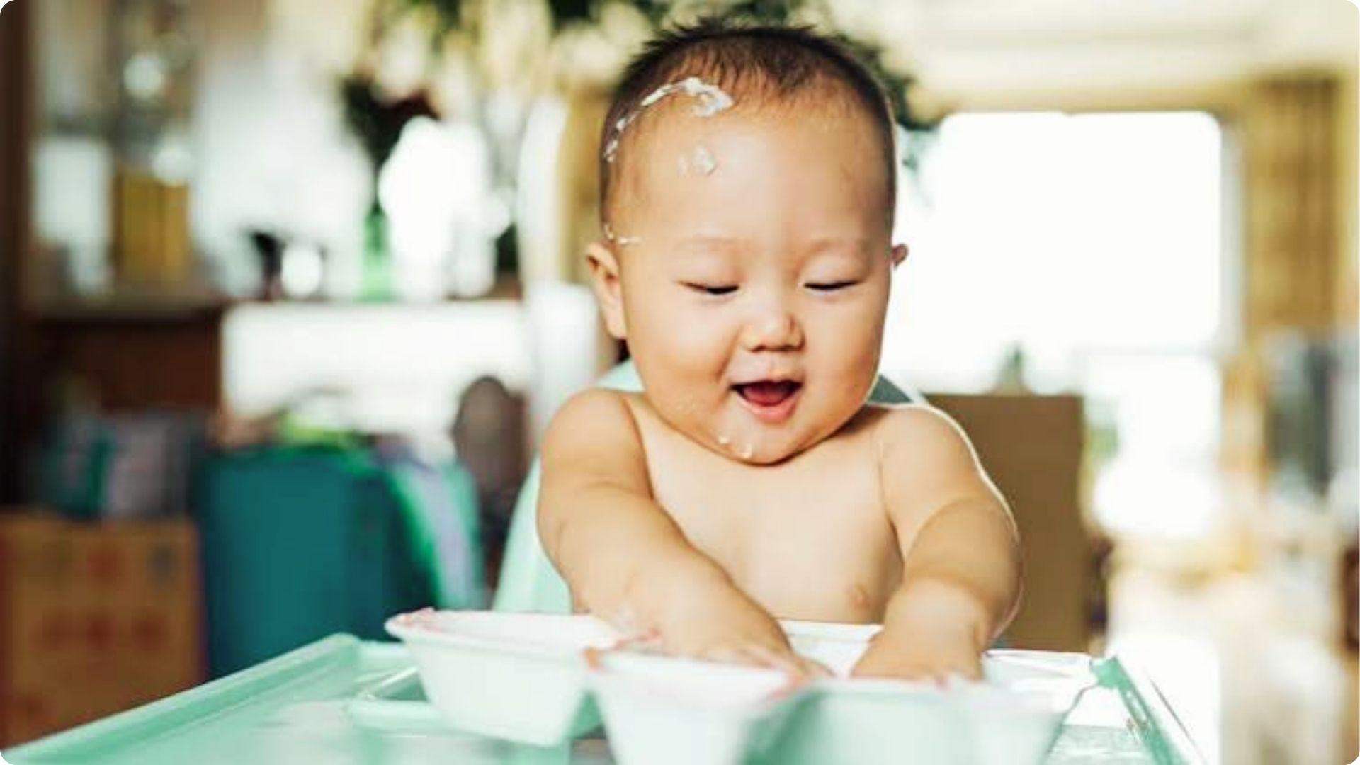 Smiling baby playing messily with rice cereal bowls, learning self-feeding after the first introduction phase.
