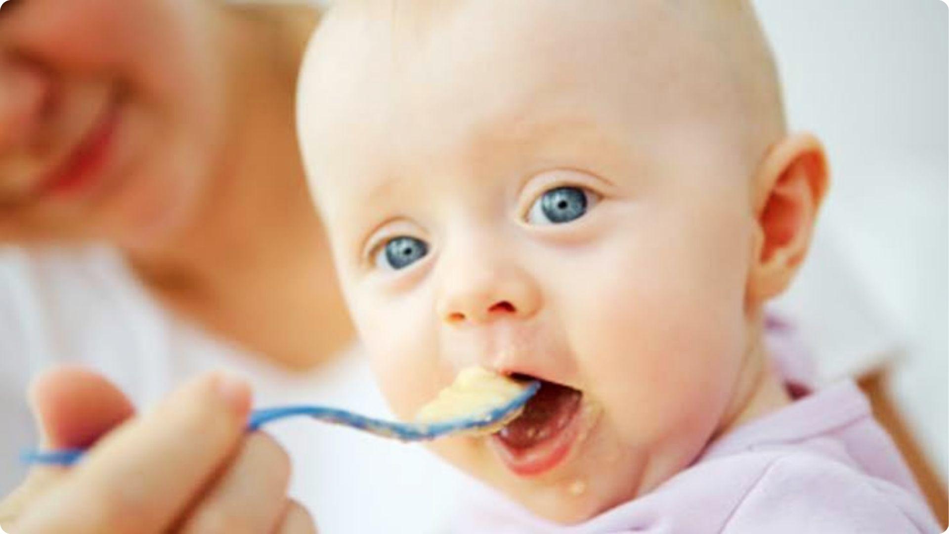 Baby happily eating the first spoon of rice cereal, ideal first food around 6 months per pediatric guidance.