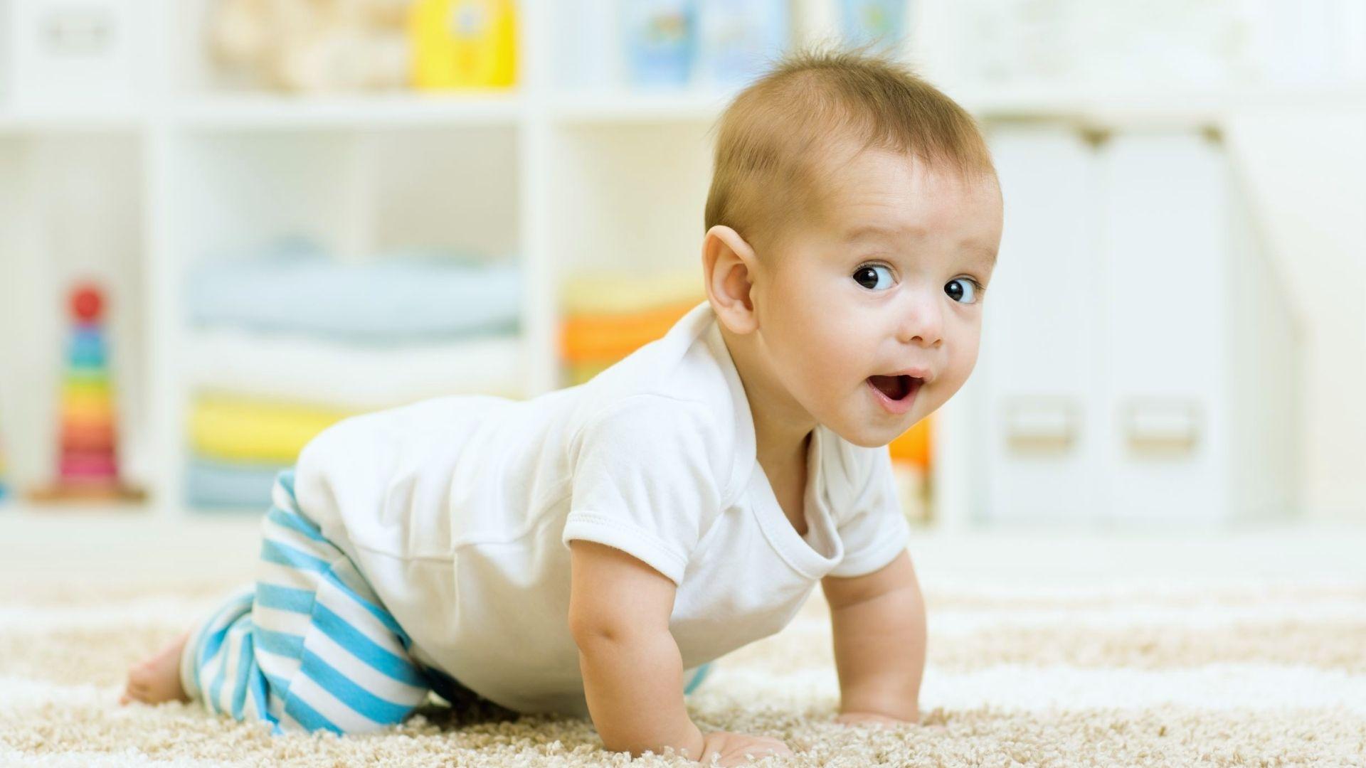Adorable baby crawling on soft carpet in bright nursery playroom with colorful toys