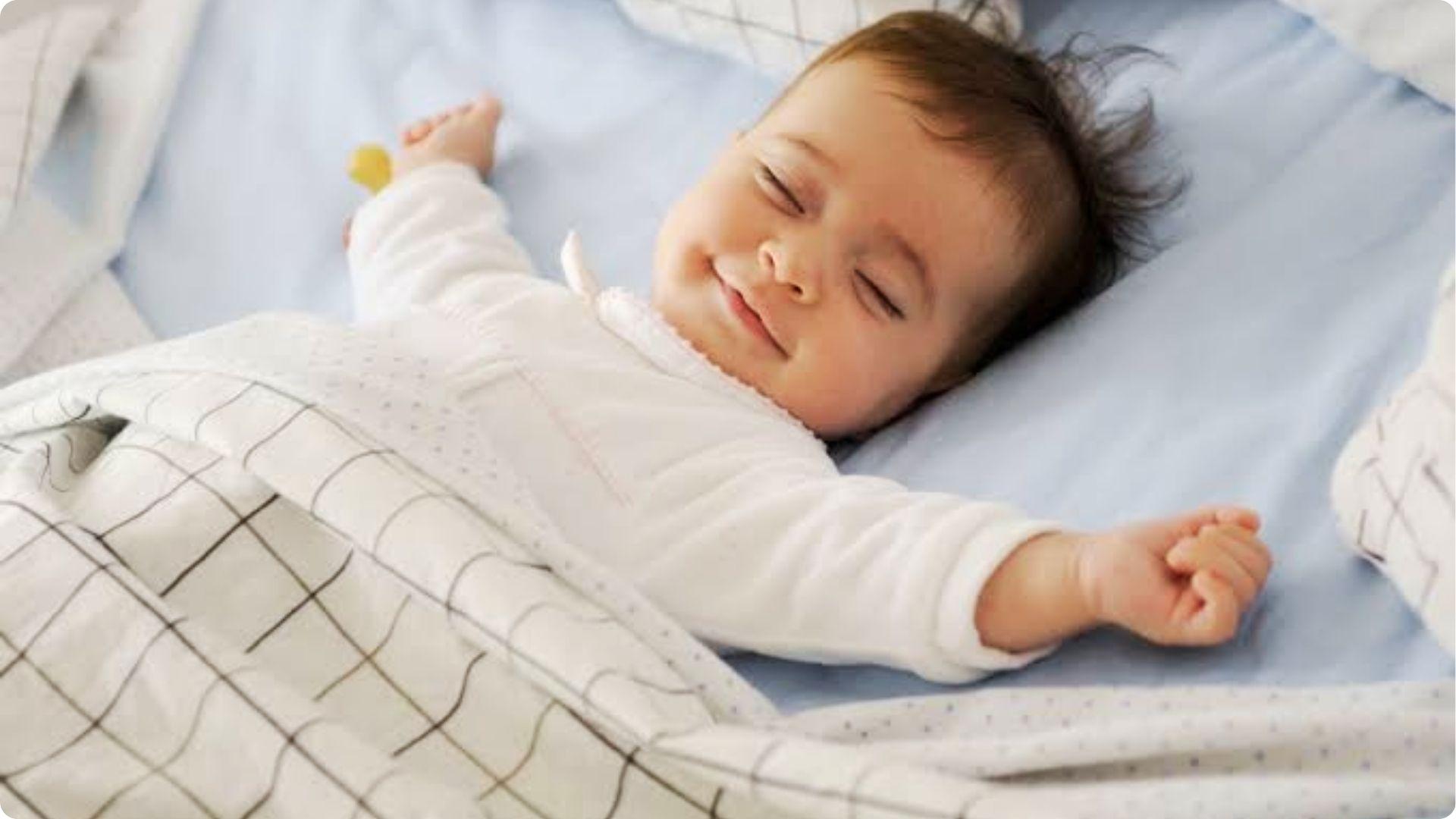 Peaceful baby in white onesie smiling on blue bedding, explains why babies smile in sleep during active REM phase