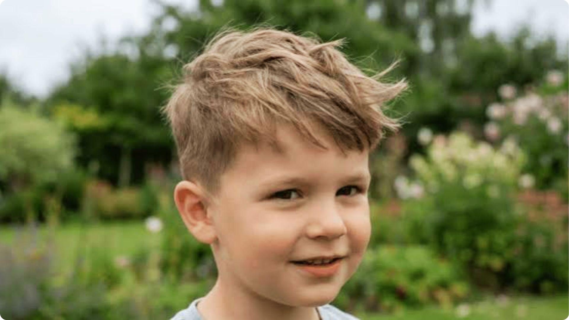 Toddler with messy textured quiff and tapered sides in garden, windswept stylish baby boy haircut.