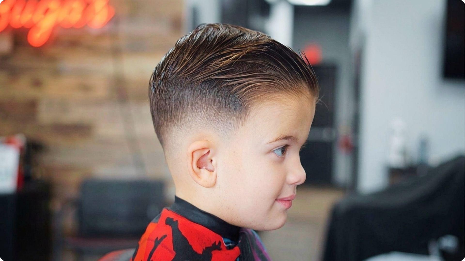 Toddler side view with slick combed-back top and high skin fade, shiny neat style, modern baby boy haircut