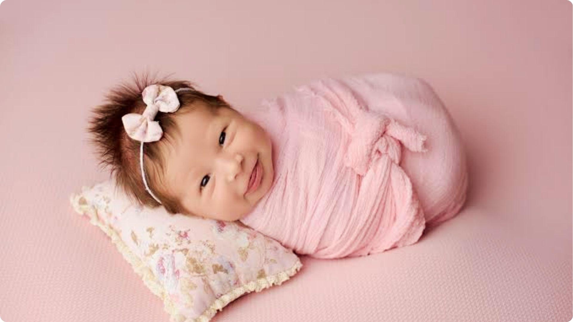 Pink swaddled baby girl with bow headband smiling, adorable example of why my baby smiles in her sleep naturally