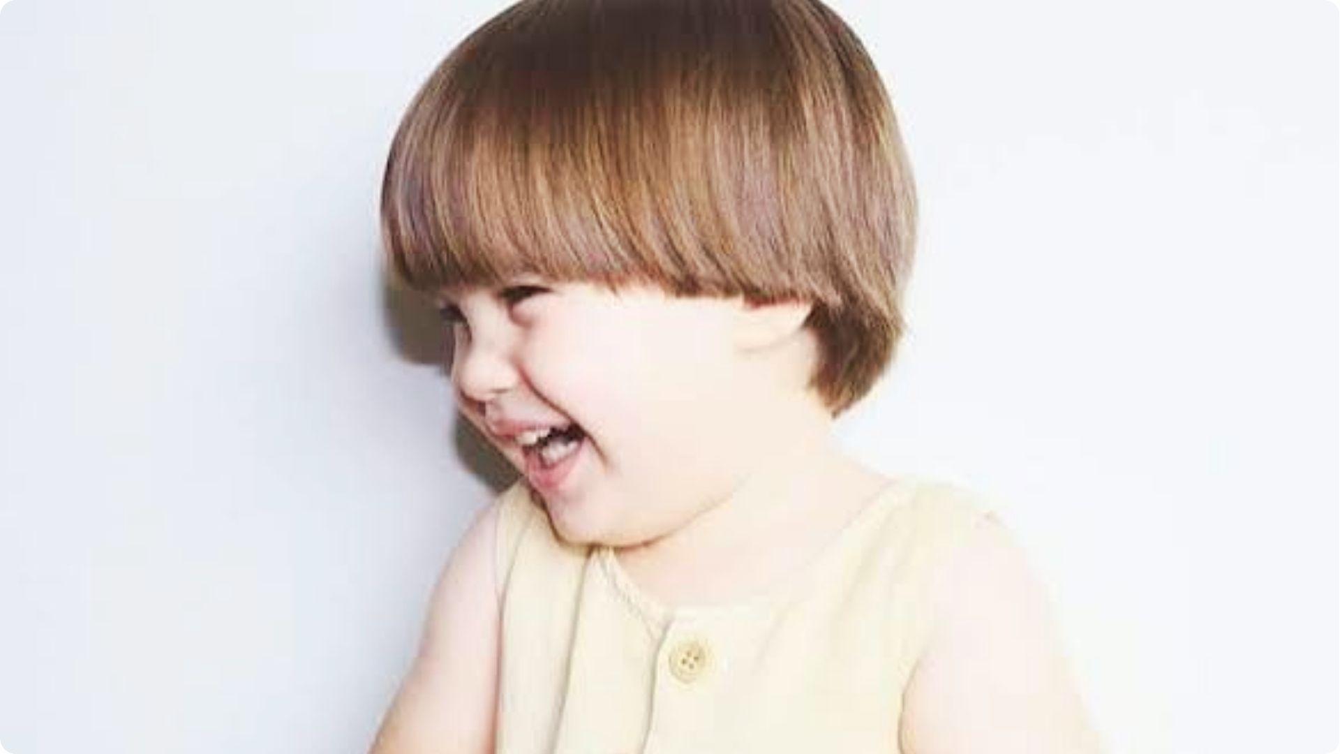 Toddler laughing with classic bowl cut and straight bangs, round shape, cute easy baby boy haircut.