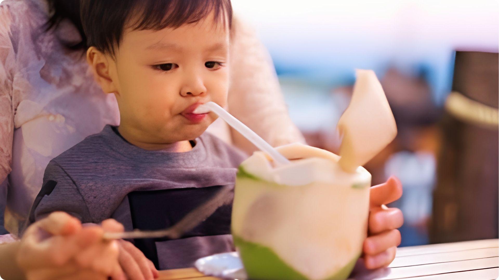 Baby boy in grey shirt drinking fresh coconut water with straw, natural hydration for infants