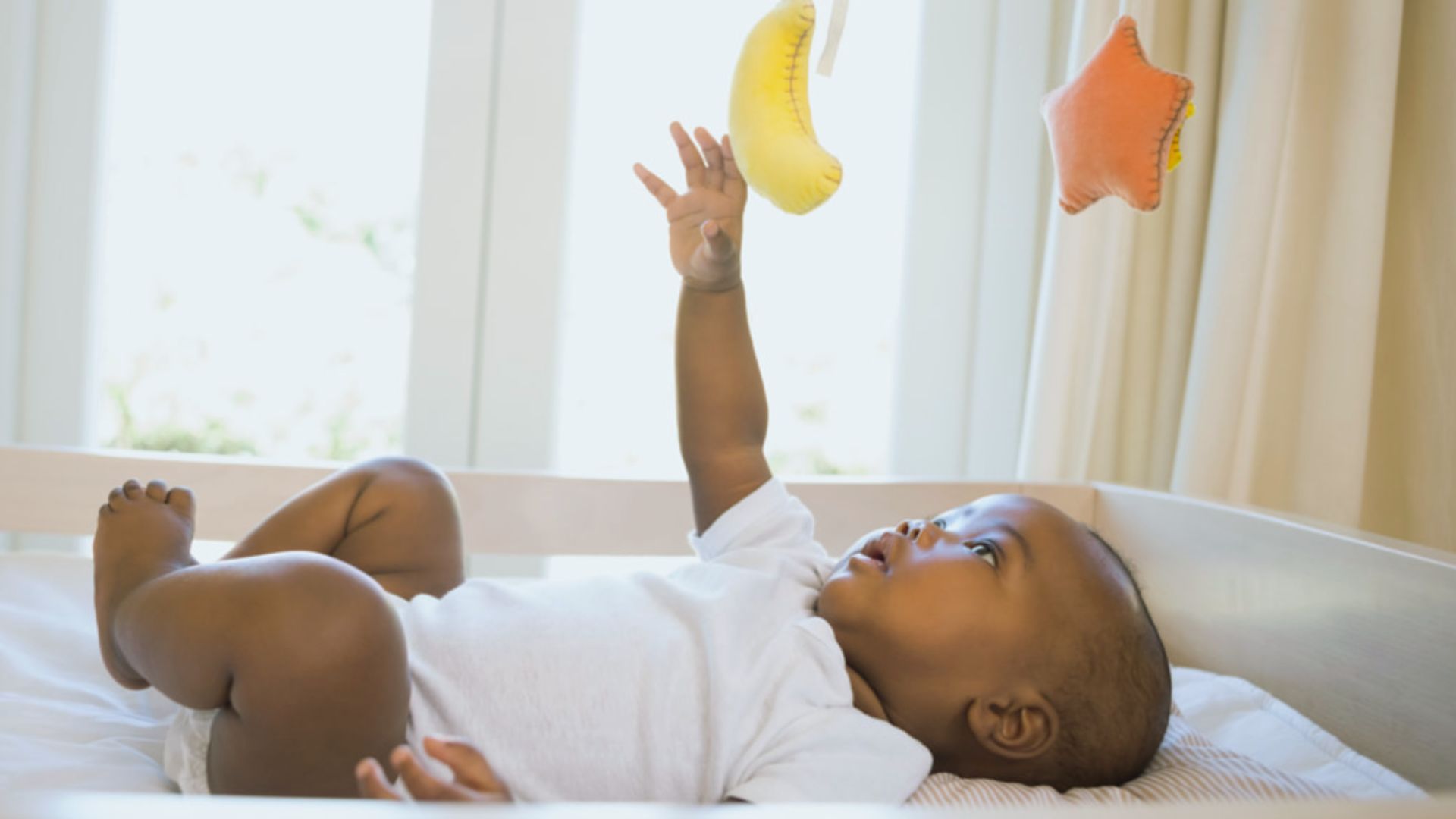 Baby lying in crib reaching for hanging moon and star plush mobile toys