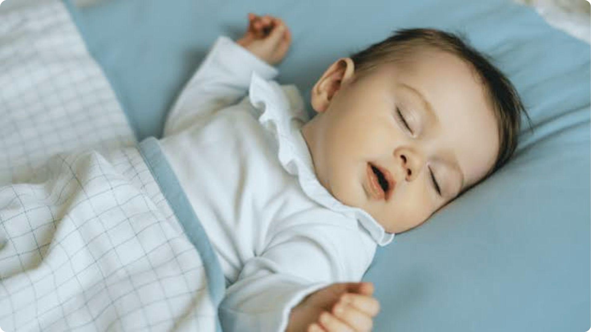 Sleeping newborn on blue pillow with soft open mouth smile, natural reflex smile during REM sleep development