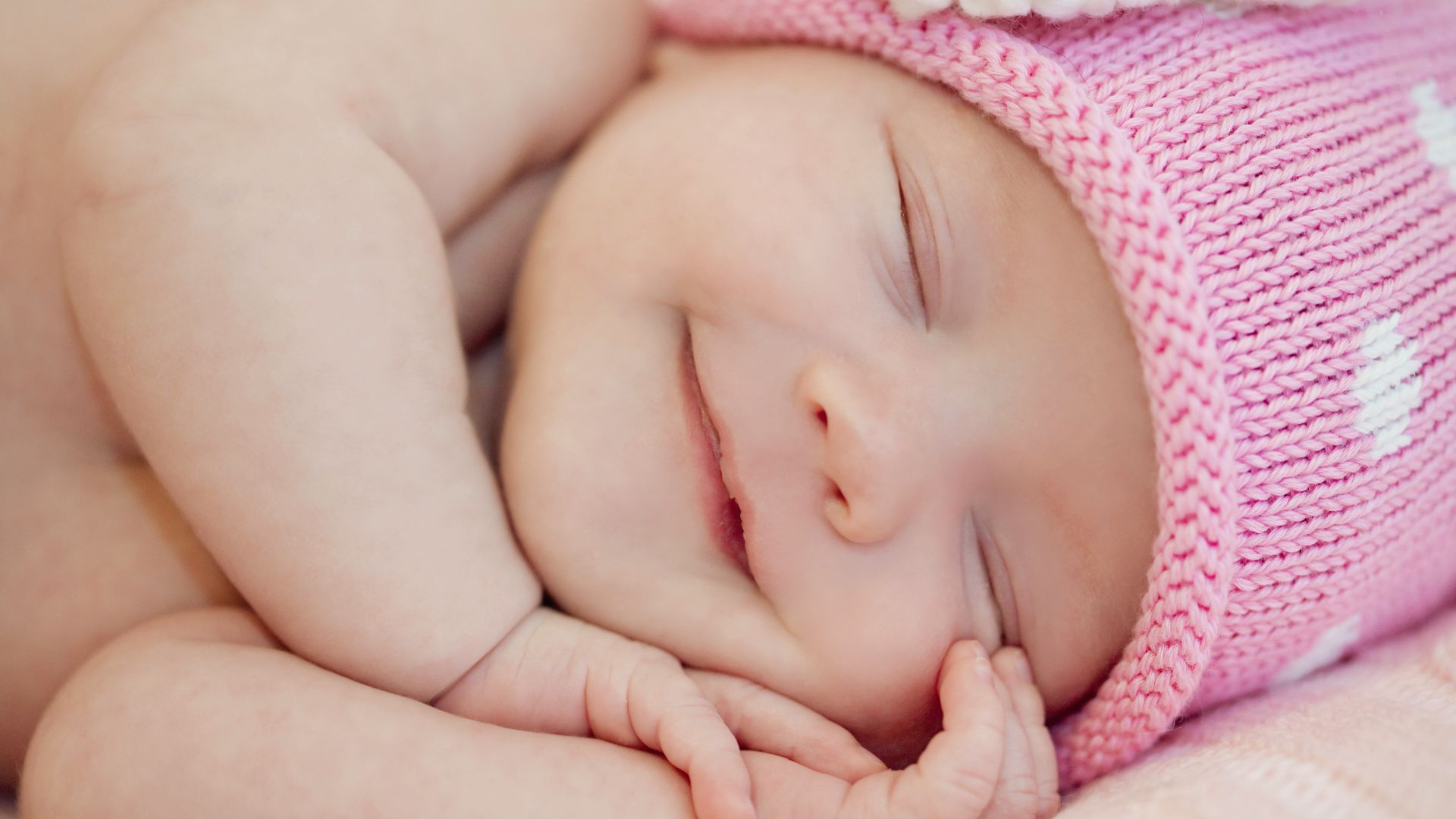 Newborn baby smiling in sleep wearing pink knitted hat with white pattern