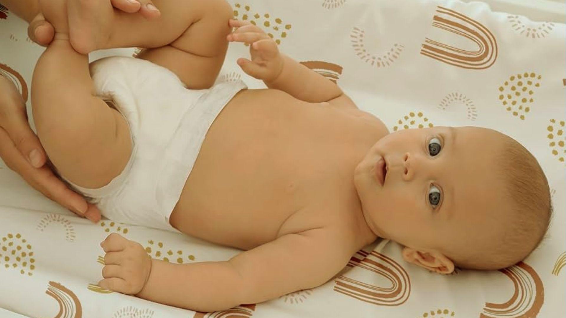 Baby in diaper lying on rainbow-patterned mat, adult hands gently holding baby's legs