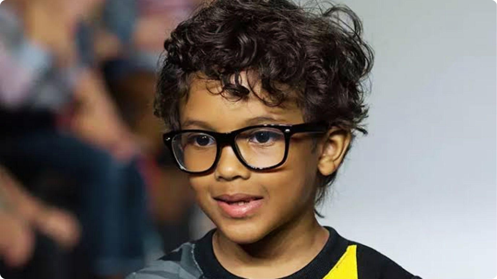 Toddler with dark curly top and short sides wearing glasses, tight curls, stylish baby boy haircut.