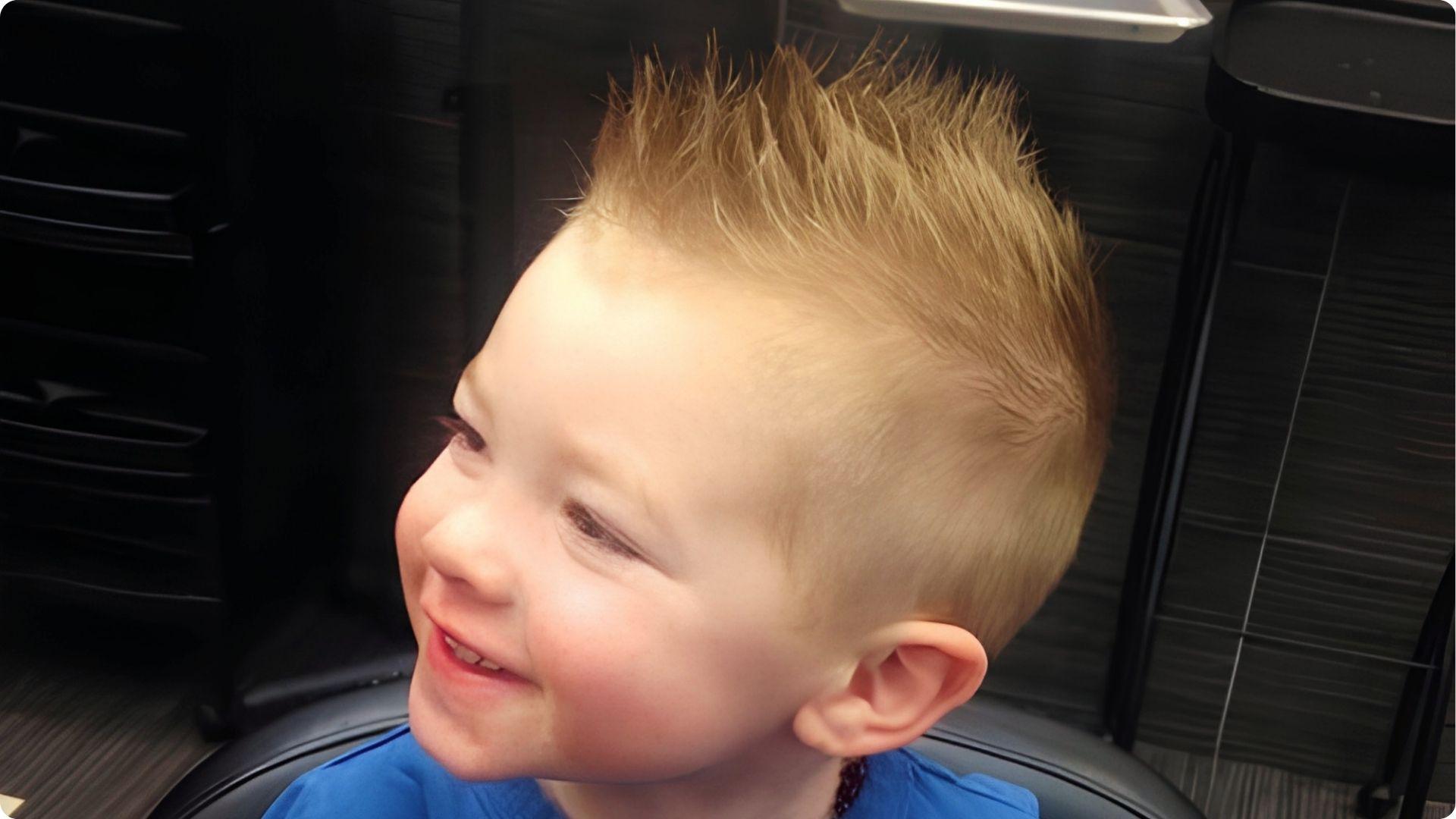 Blonde toddler with spiky mohawk top and short faded sides, playful cute baby boy haircut in salon.