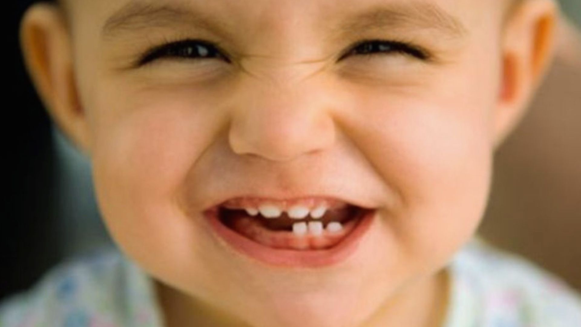 Close-up of giggling baby with squinted eyes and big grin showing upper and lower baby teeth