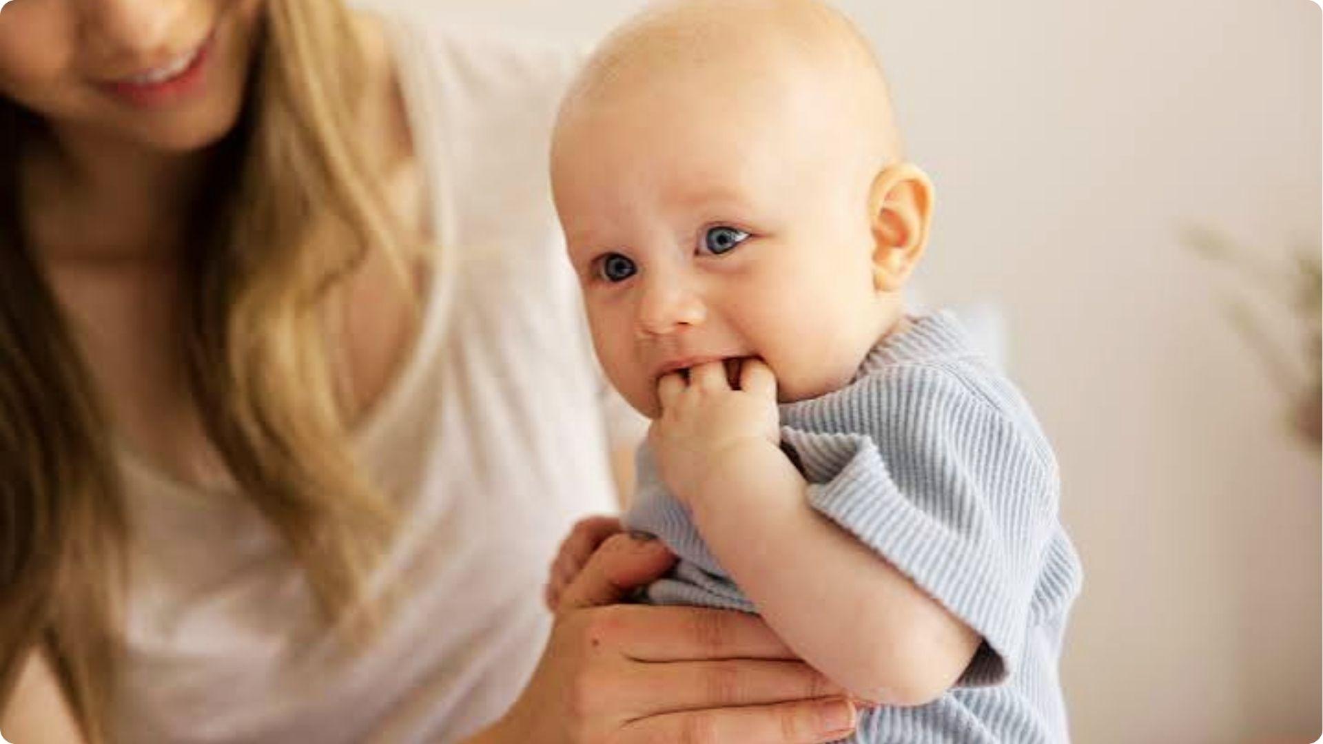 Baby in mother's arms sucking fingers, a natural reflex that often begins before birth and early infancy