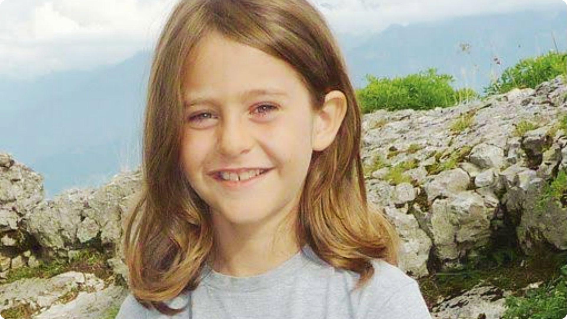 Child with long straight center-part hair past shoulders, soft wavy ends, outdoor rocky background