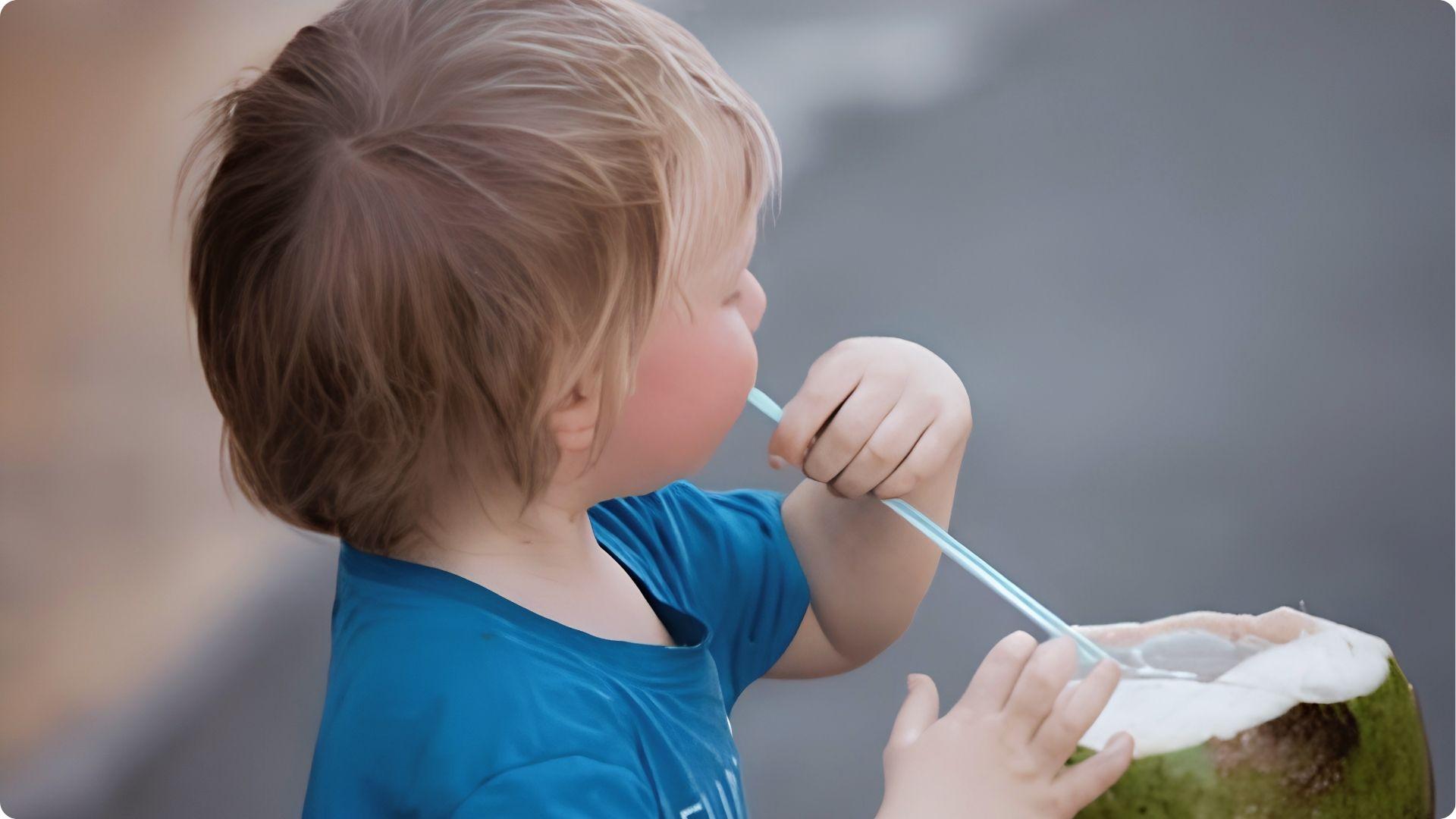 Toddler in blue shirt drinking fresh coconut water with straw, safe natural hydration for babies