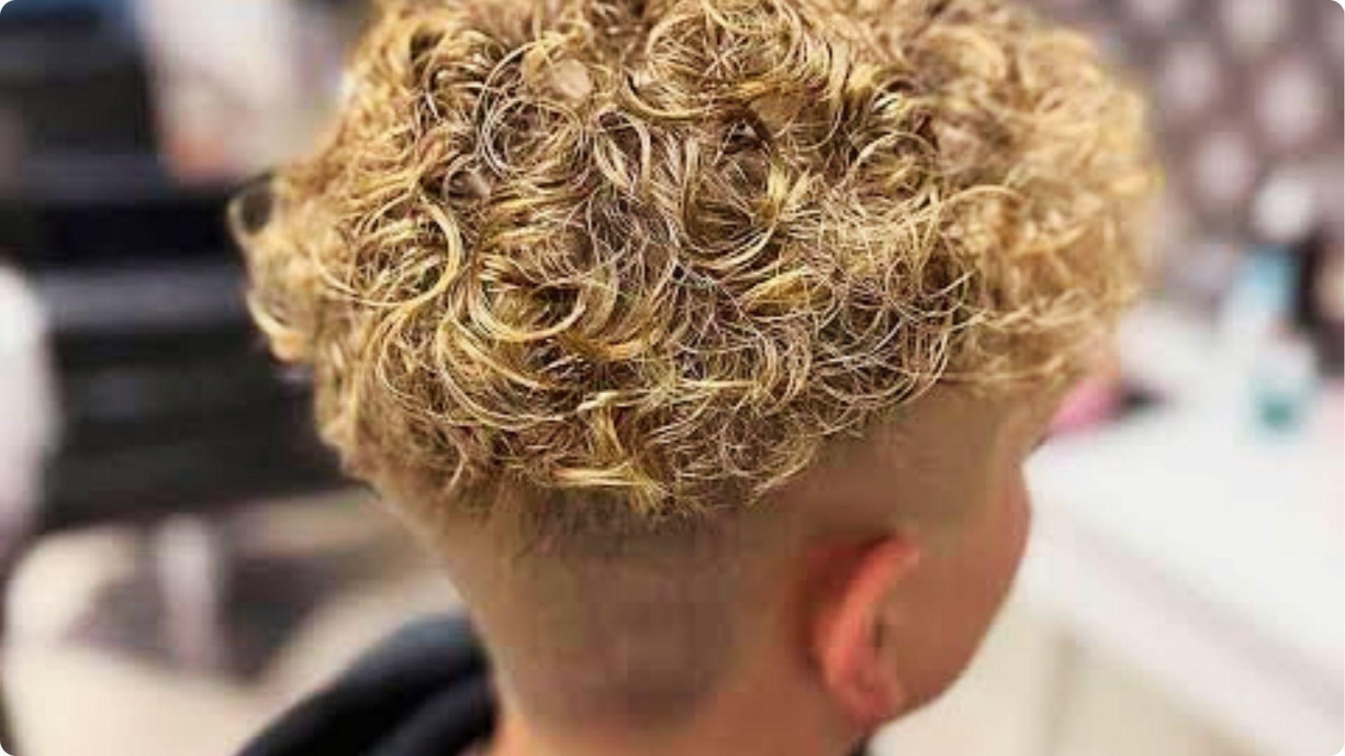 Toddler in denim jacket with curly top and temple fade with shaved line, cool modern baby boy cut.
