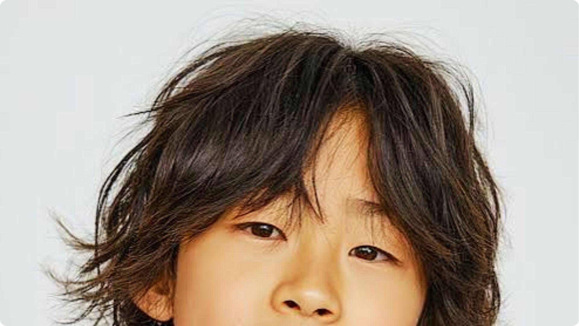 Child with tousled middle-parted wavy hair and curtain bangs, messy layered top, casual boy haircut