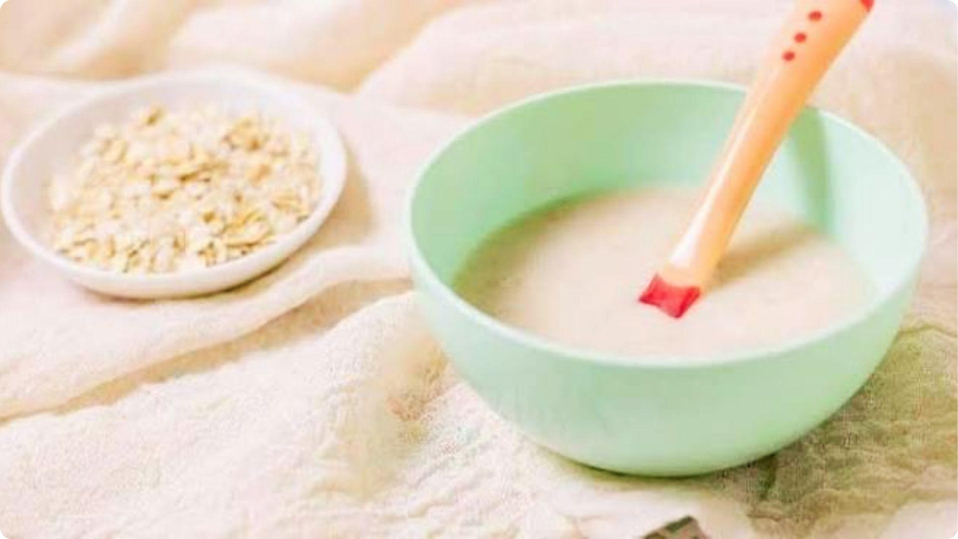 Green bowl of creamy rice cereal puree with oats, common starter food when baby sits with support.