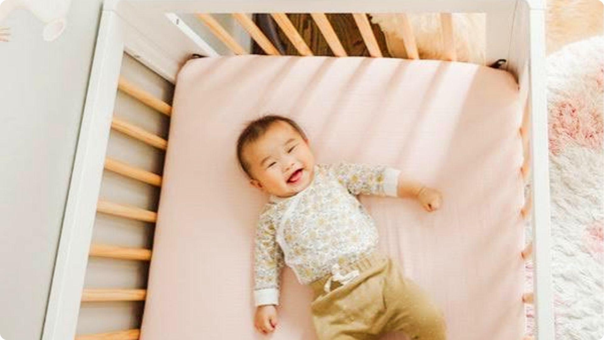 Joyful baby laughing in crib on pink sheet, involuntary smile reflecting healthy brain development in sleep cycle