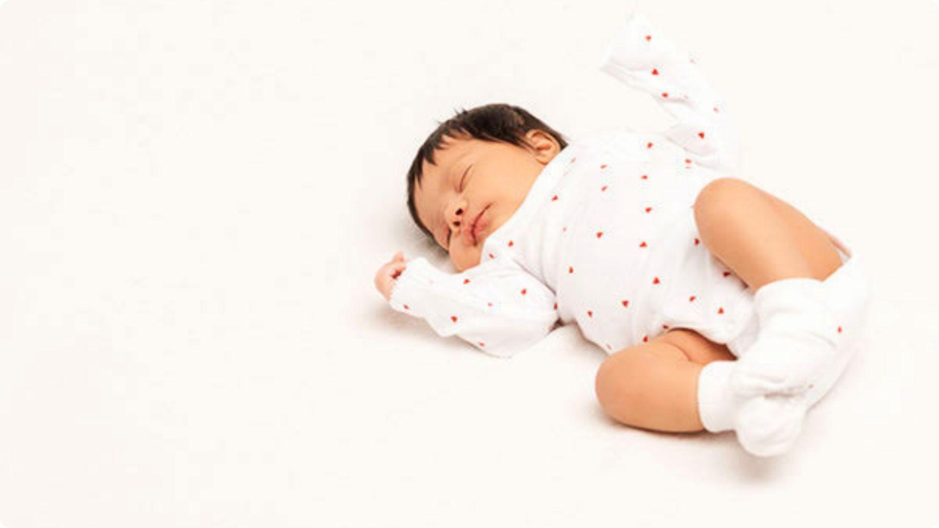 Newborn in heart print onesie sleeping sideways smiling, common reflex smile as nervous system matures in sleep