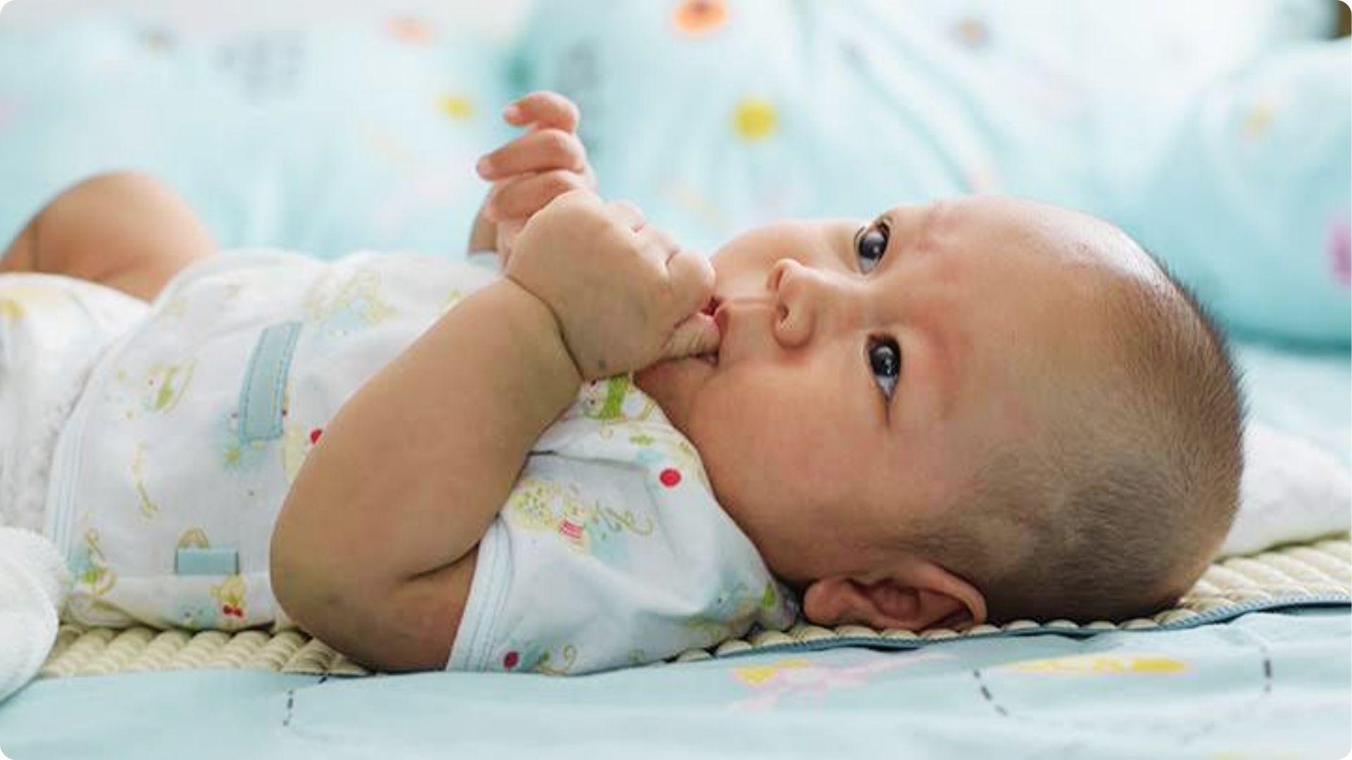 Infant lying on bed sucking thumb, displaying early self soothing habit that begins in first weeks of life