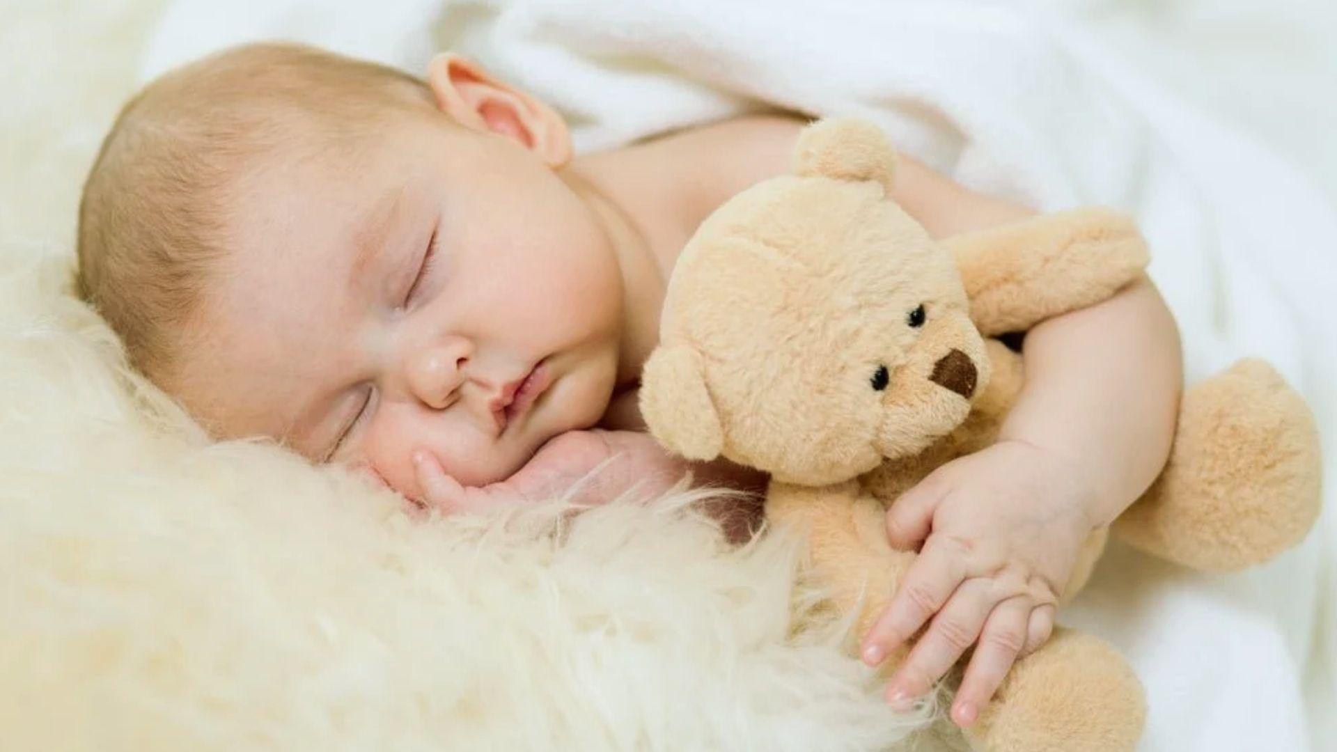 Newborn baby sleeping peacefully cuddling teddy bear on soft fluffy white blanket