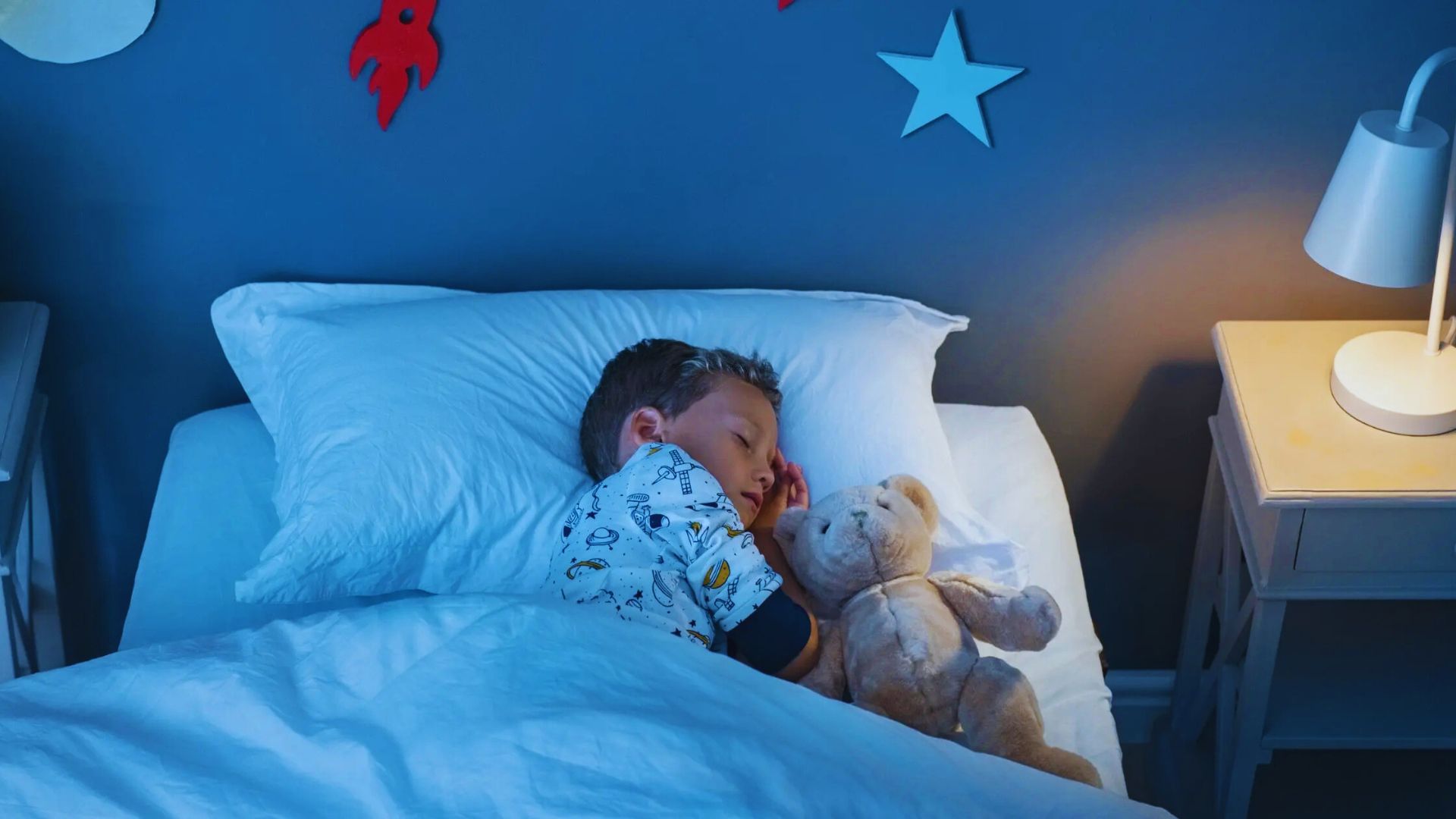 A child resting in bed with a teddy bear, eyes closed, in a serene sleeping position.