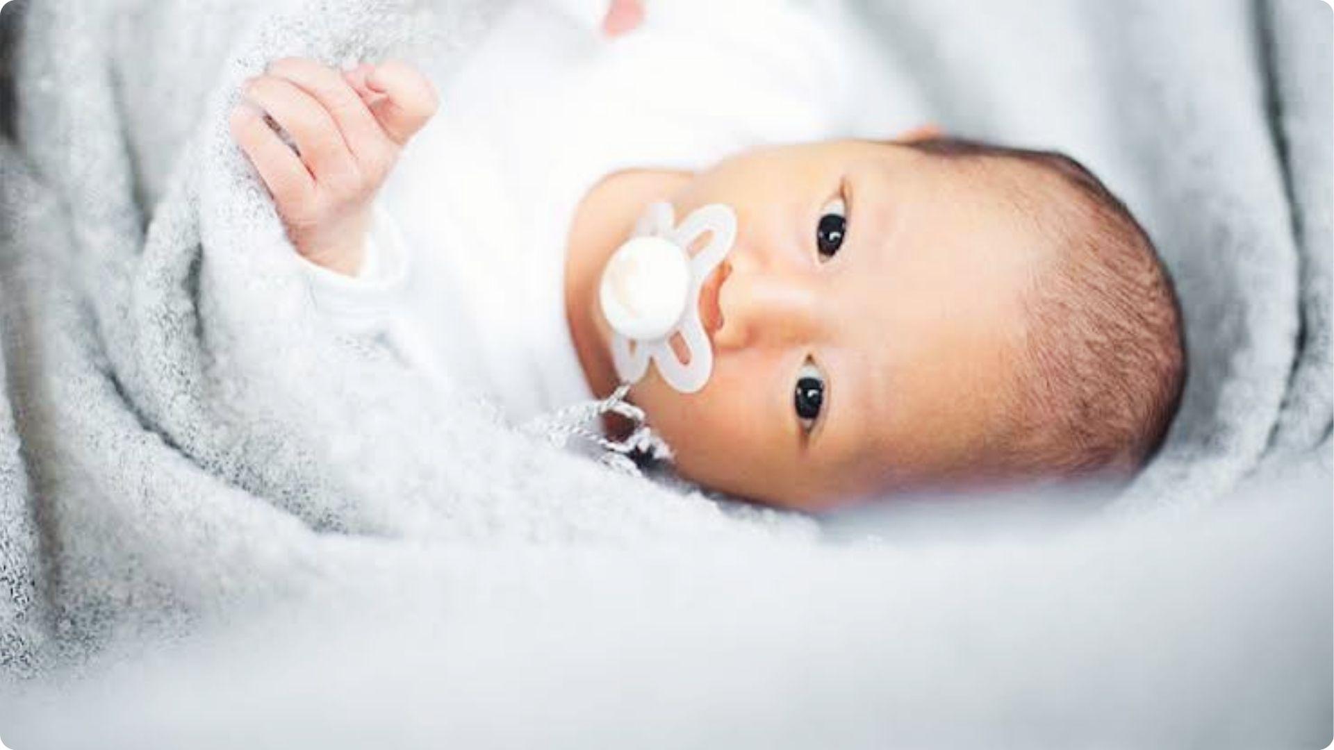 Awake infant with white pacifier on gray blanket, showing pacifiers calm and soothing babies gently.