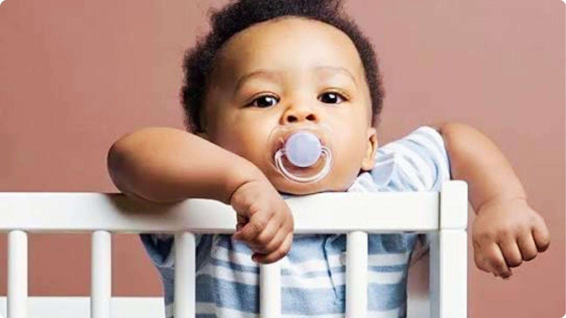 Baby with purple pacifier leaning on crib rail, showing pacifier use for infant comfort and safety.