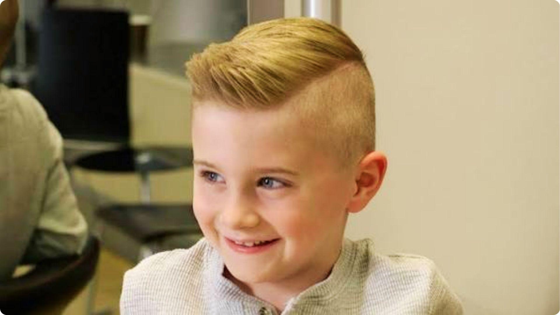 Blonde toddler with soft side-swept layered hair and side part, wavy top, cute natural baby boy cut.