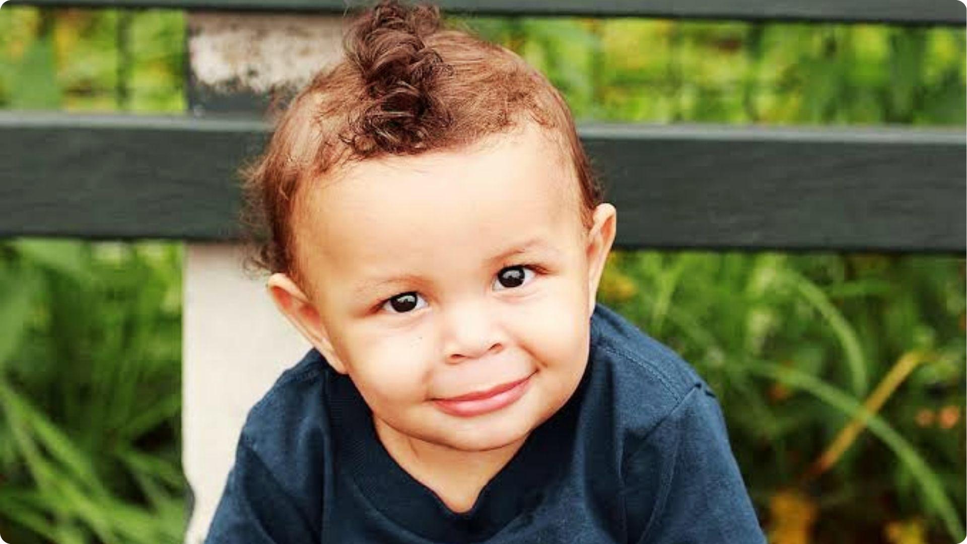 Baby with curly faux hawk and shaved sides, cute curly top knot, playful baby boy haircut style.