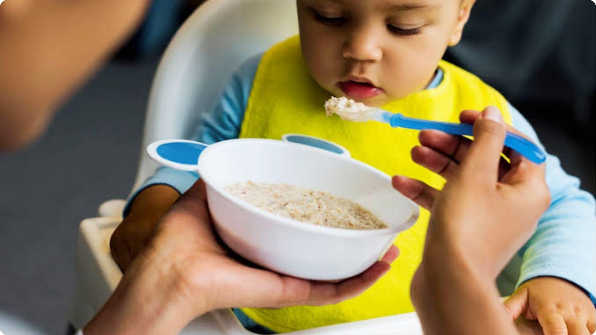 Caregiver feeding rice cereal to infant in highchair, starting when baby has good head control.