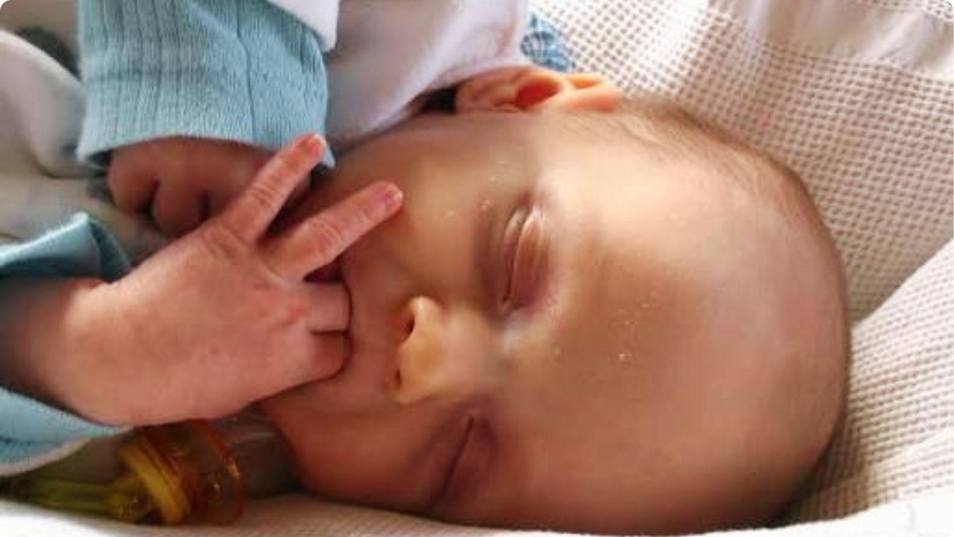 Newborn baby sleeping with hand in mouth, illustrating thumb sucking that starts in utero development