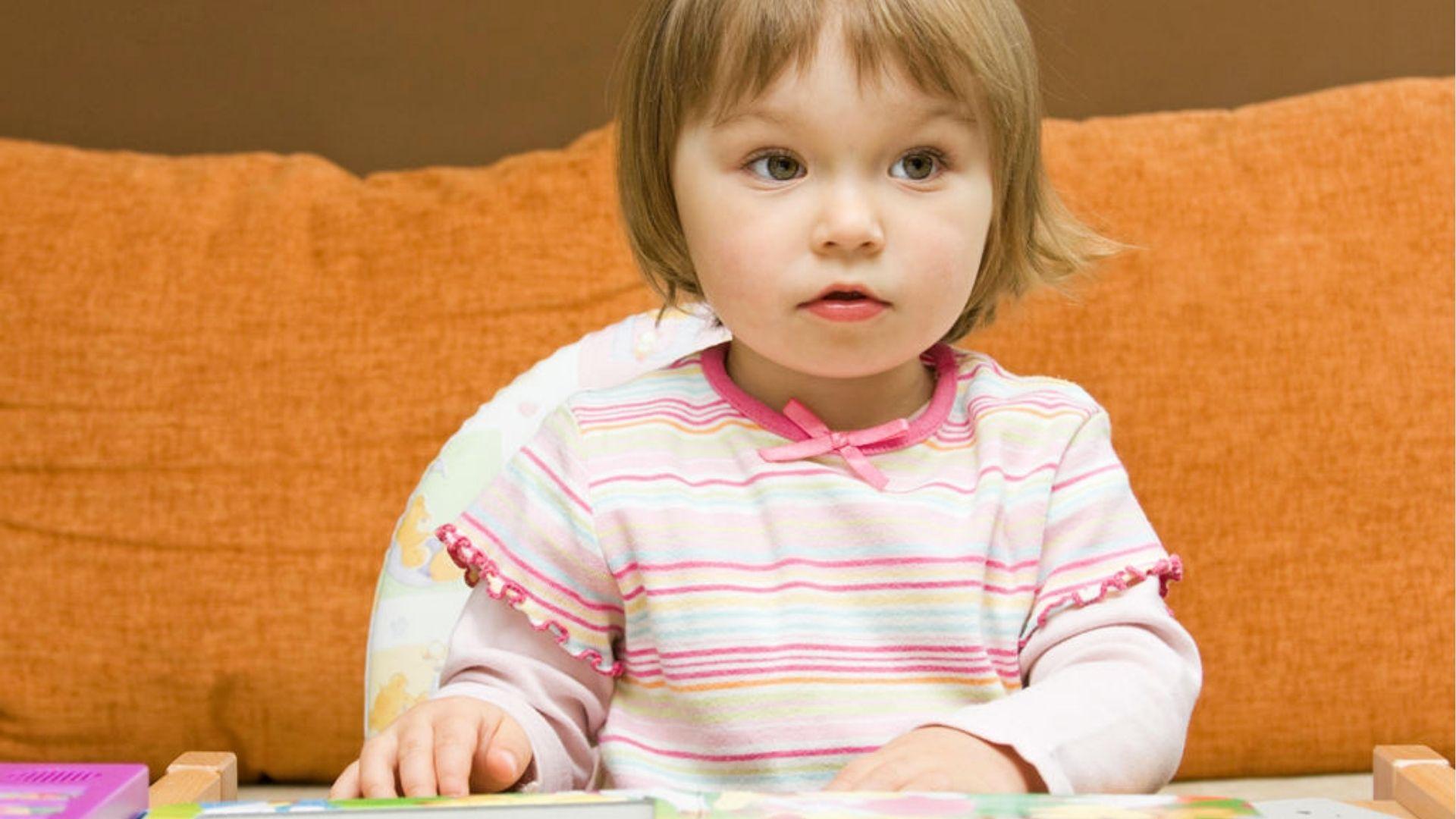 20-month-old girl in high chair listening closely.