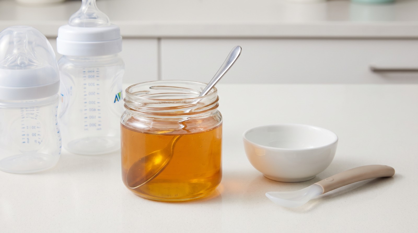 Jar of honey and spoon beside infant feeding items