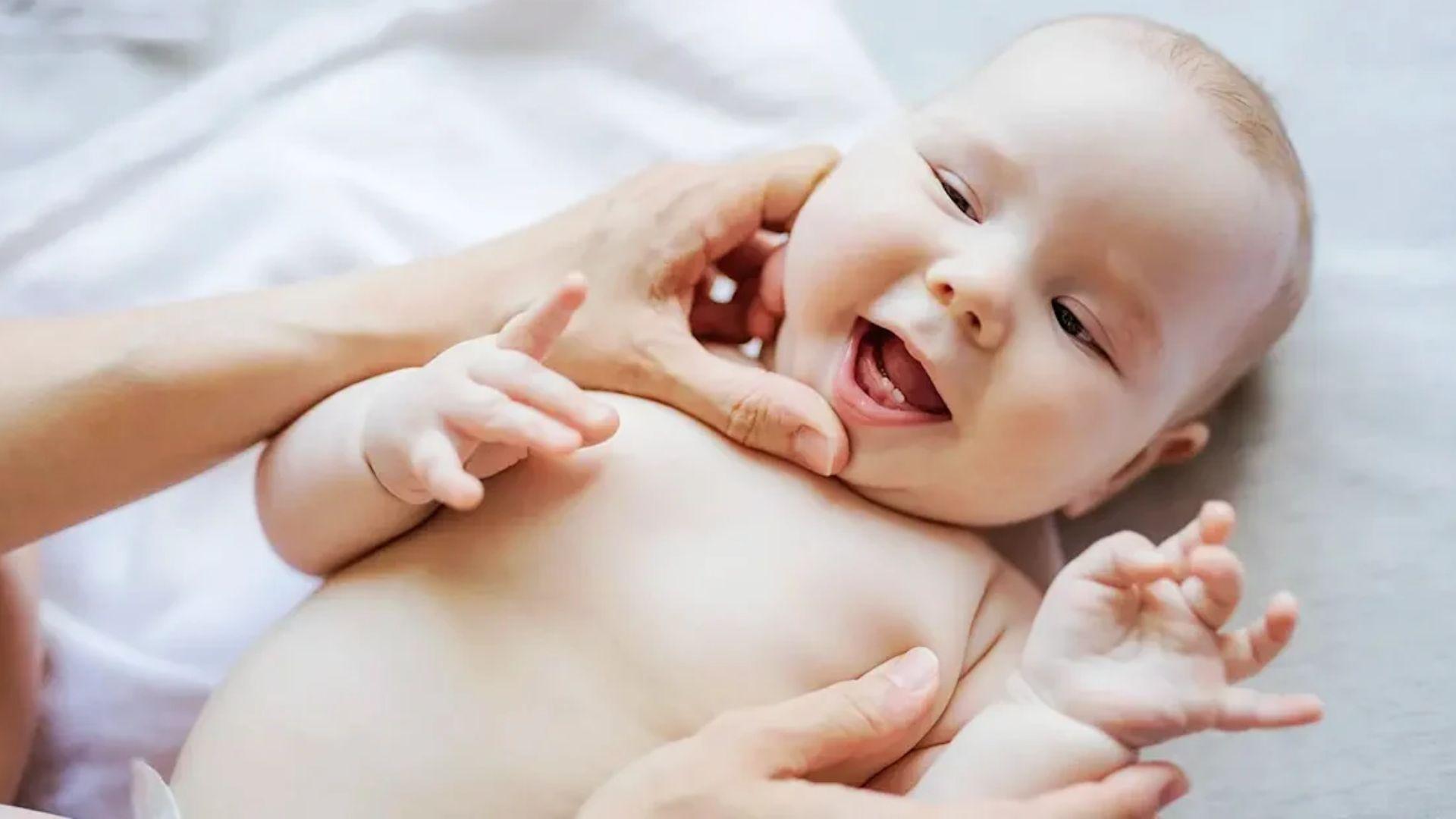 Cheerful baby lying on bed laughing with lower teeth visible.