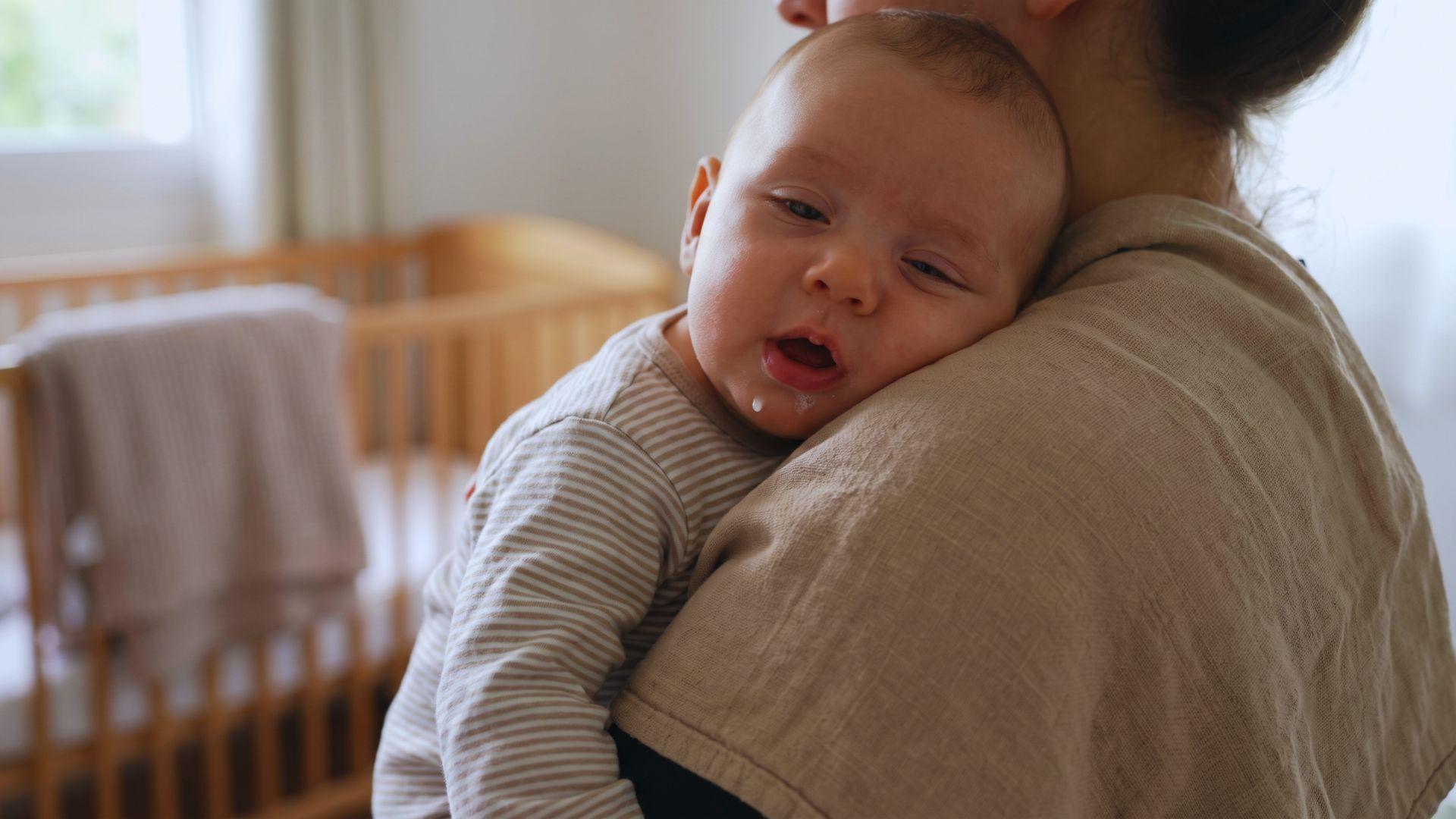 Baby held upright against a cloth-covered shoulder after feeding, with the mouth slightly open.