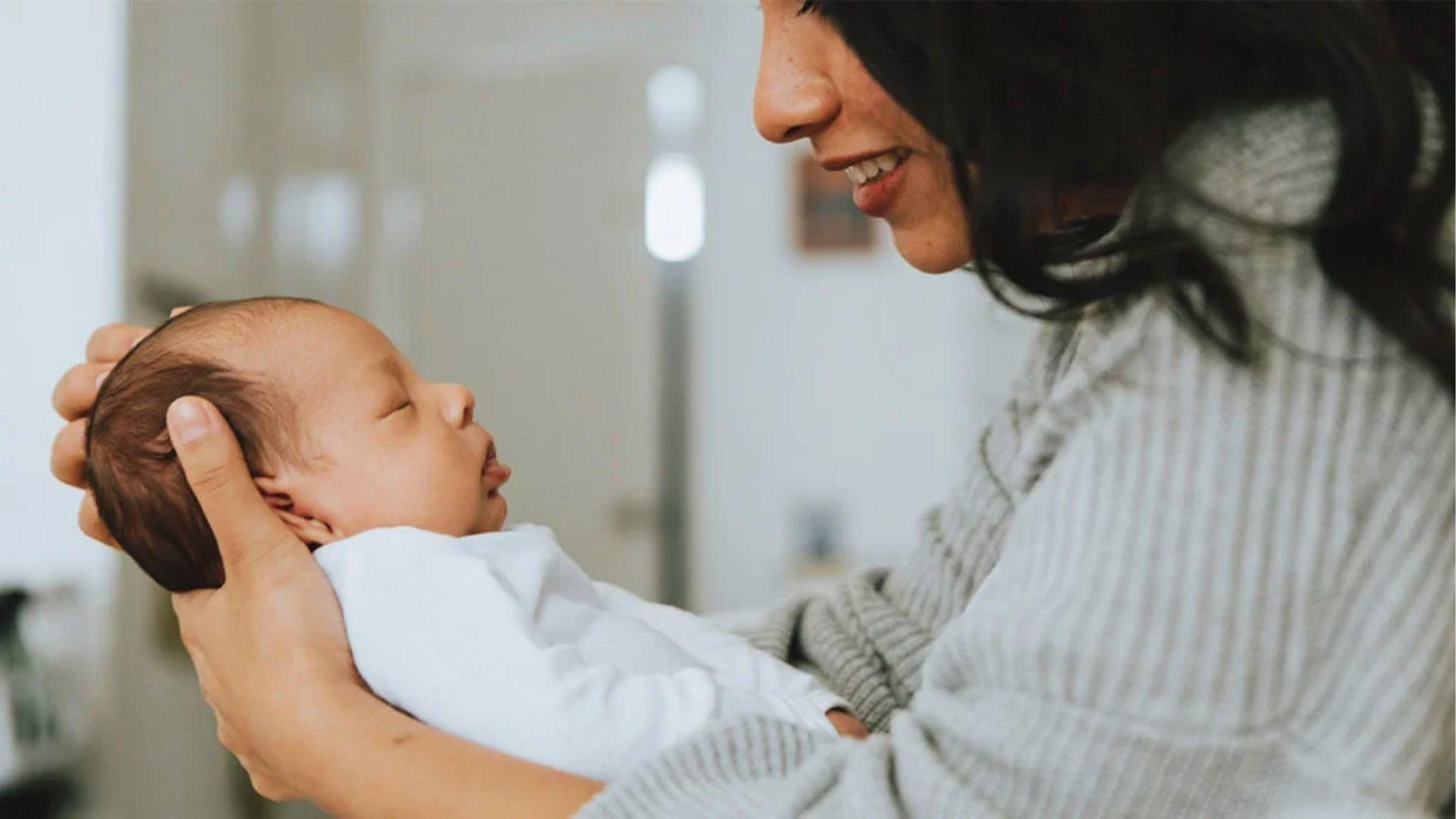 Smiling mother cradles sleeping newborn peacefully.