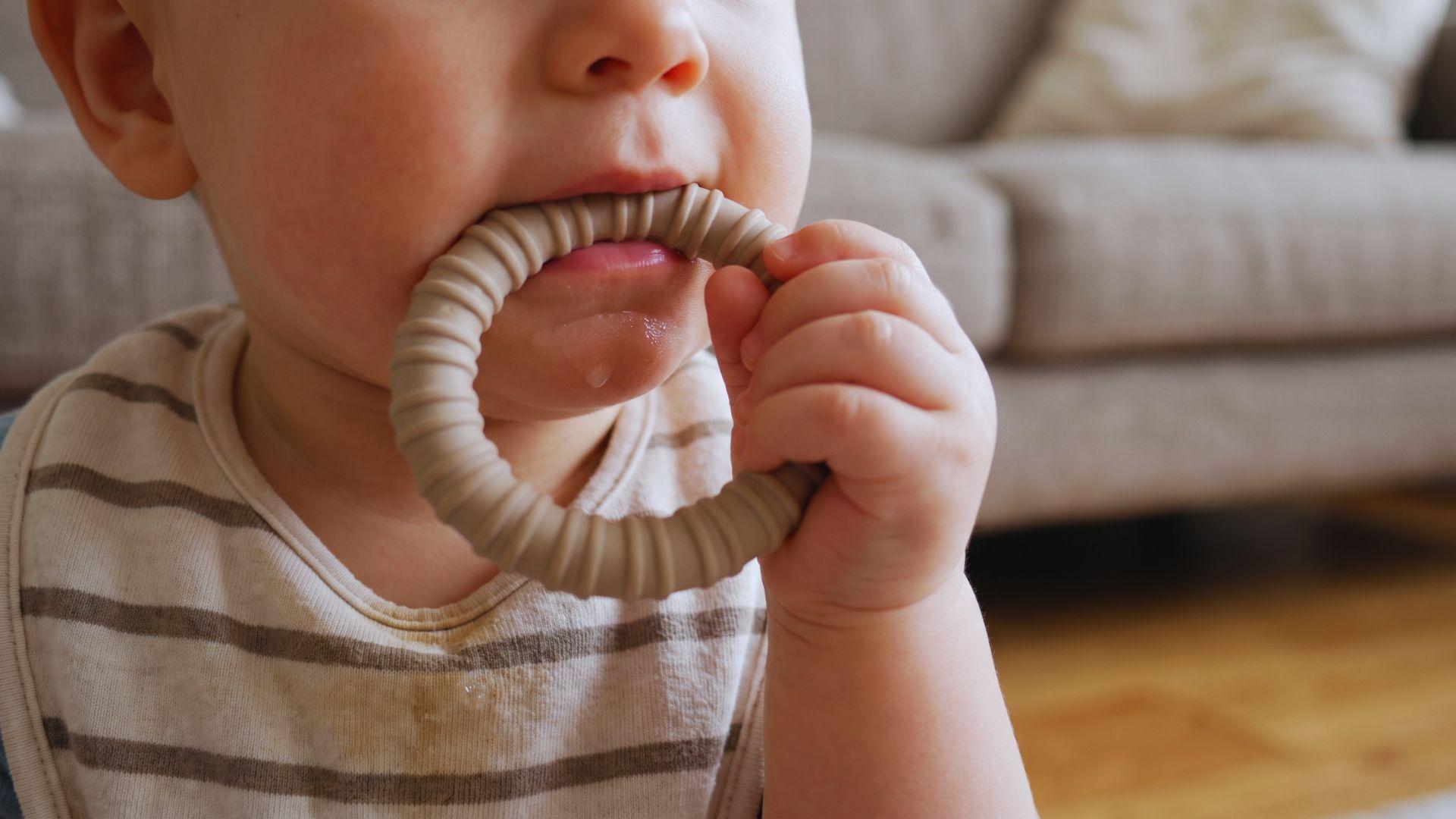 Baby mouthing a teething toy with saliva on the chin.