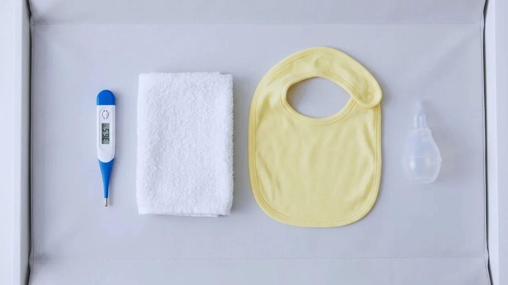 Digital thermometer, washcloth, baby bib, and nasal aspirator arranged on a clean surface.
