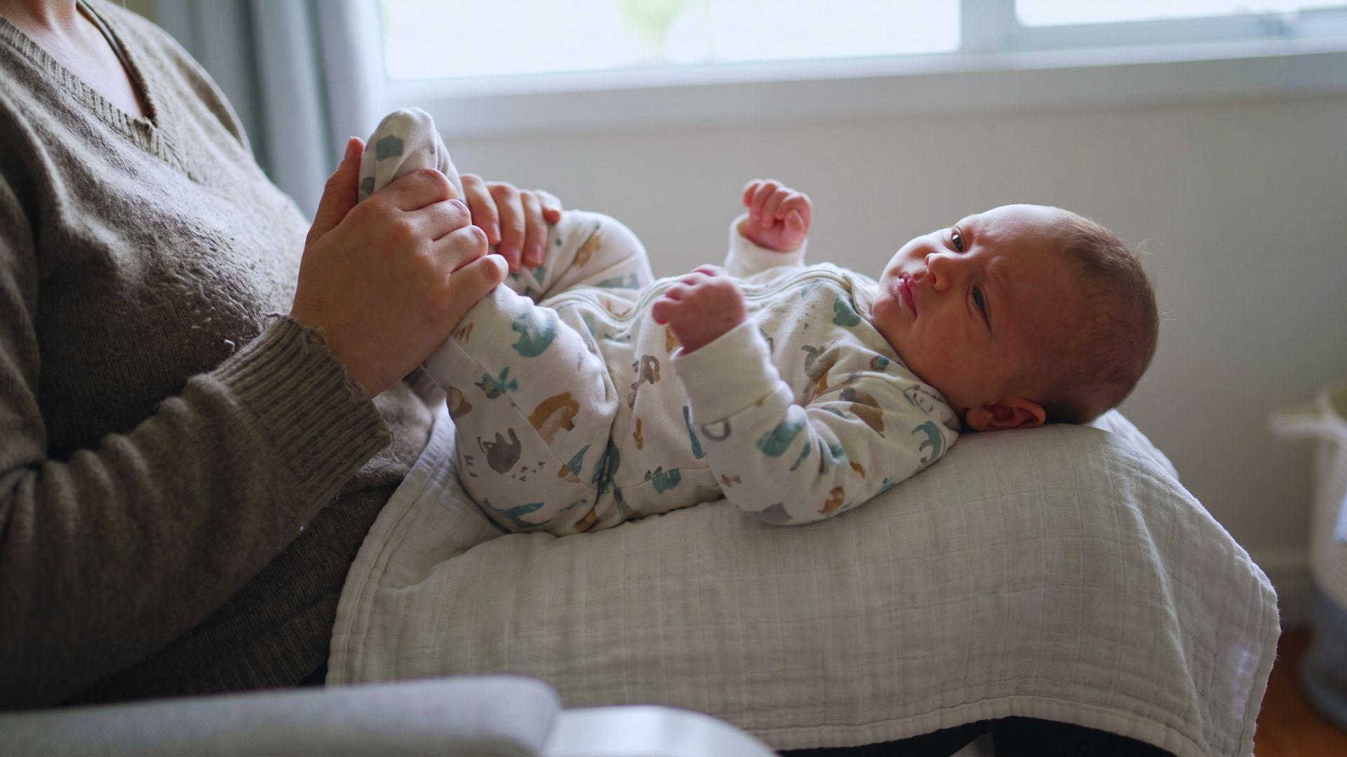 Parent gently supporting a baby’s bent legs as the infant draws their knees toward the belly.
