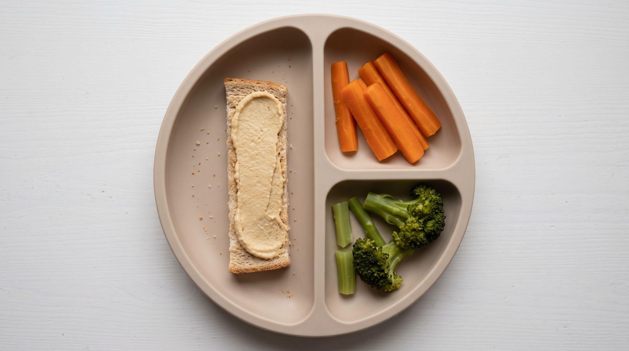 Hummus spread on soft toast beside steamed carrot and broccoli batons