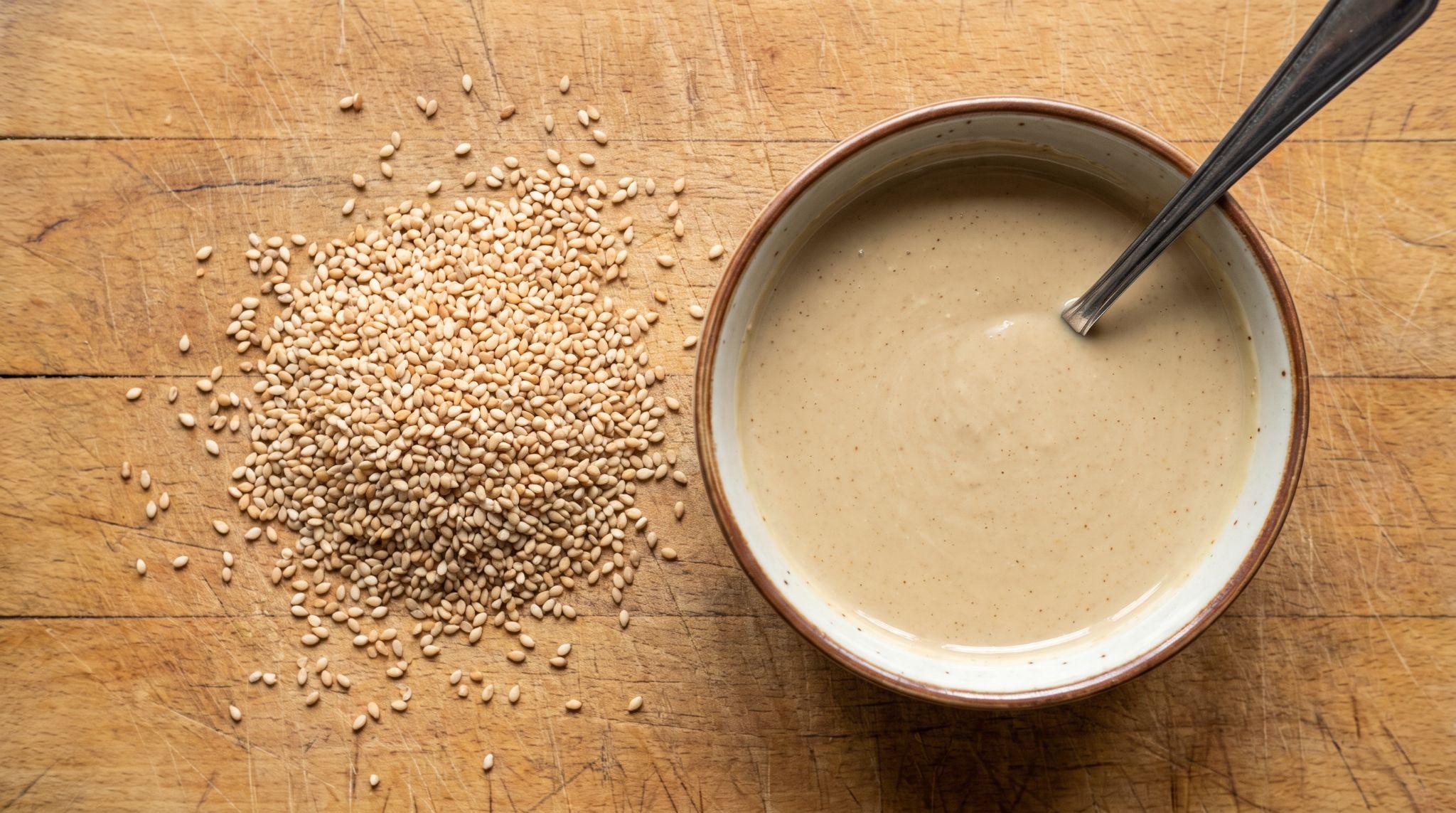 Tahini in a small bowl beside sesame seeds
