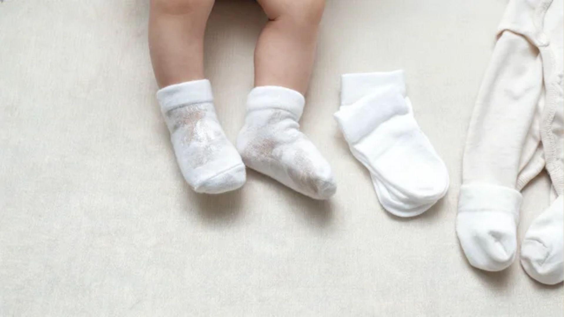 Damp cotton baby socks beside dry socks and a cotton footed sleeper on a nursery surface