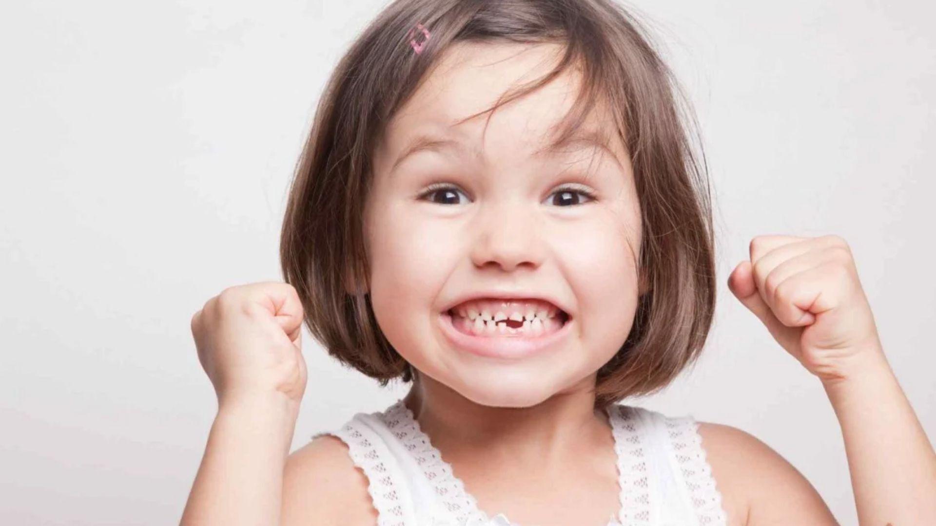 Child clenching teeth with visible uneven baby teeth and raised fists.