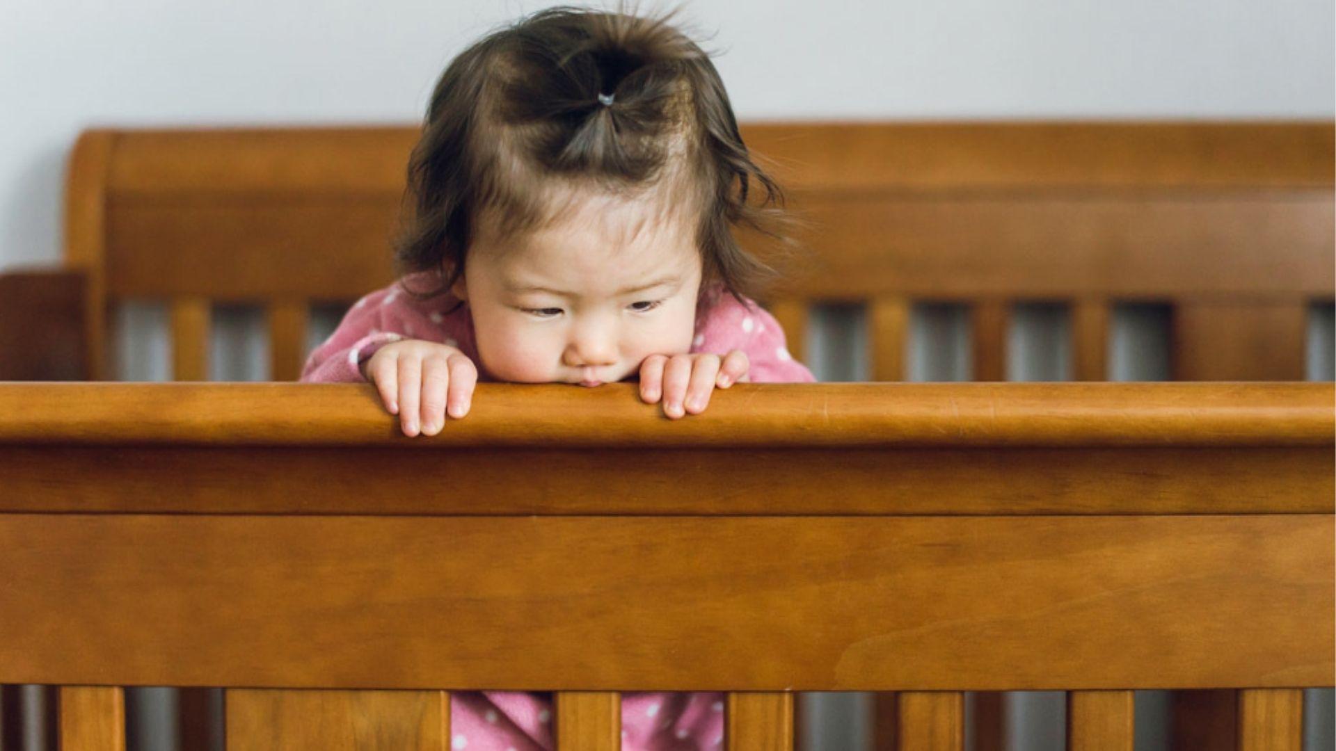 Child standing in a crib and holding the wooden rail