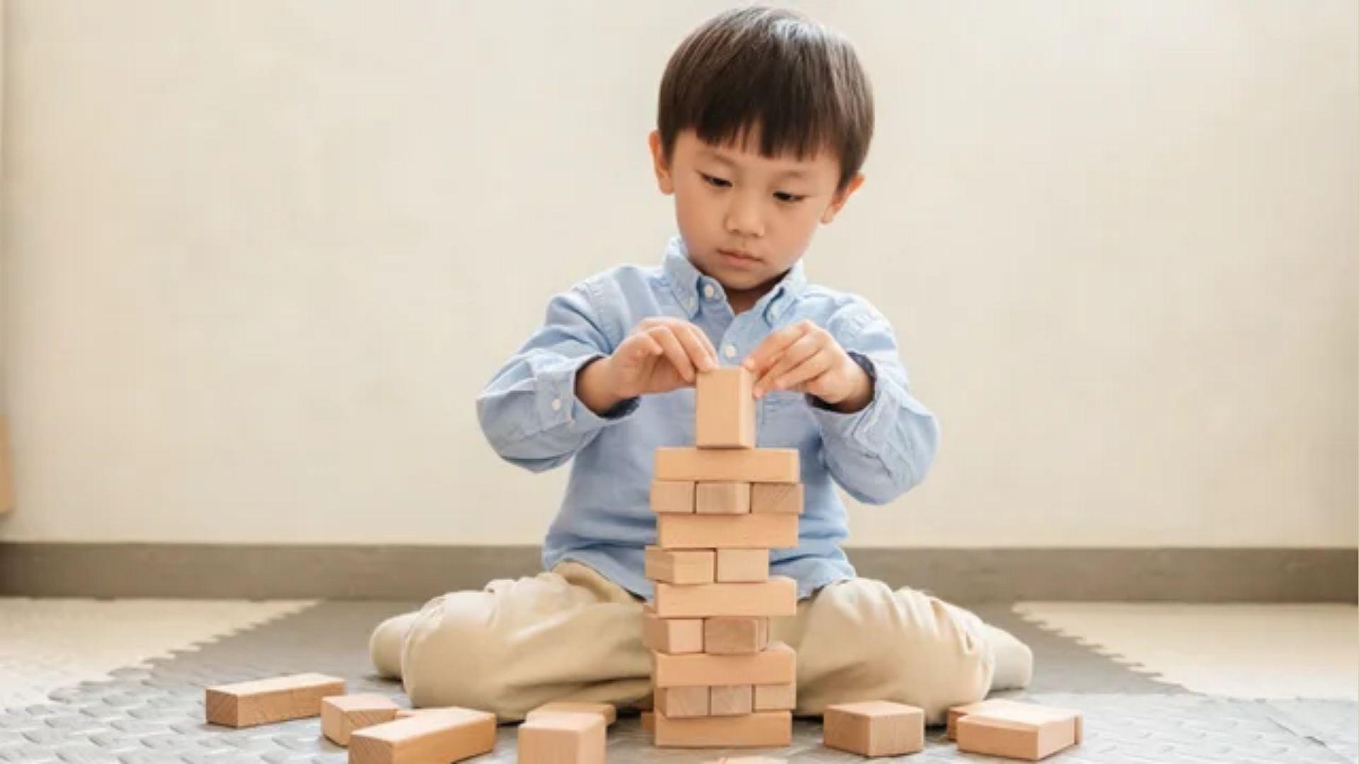 Young child rebuilding a wooden block tower while loose blocks lie on the floor