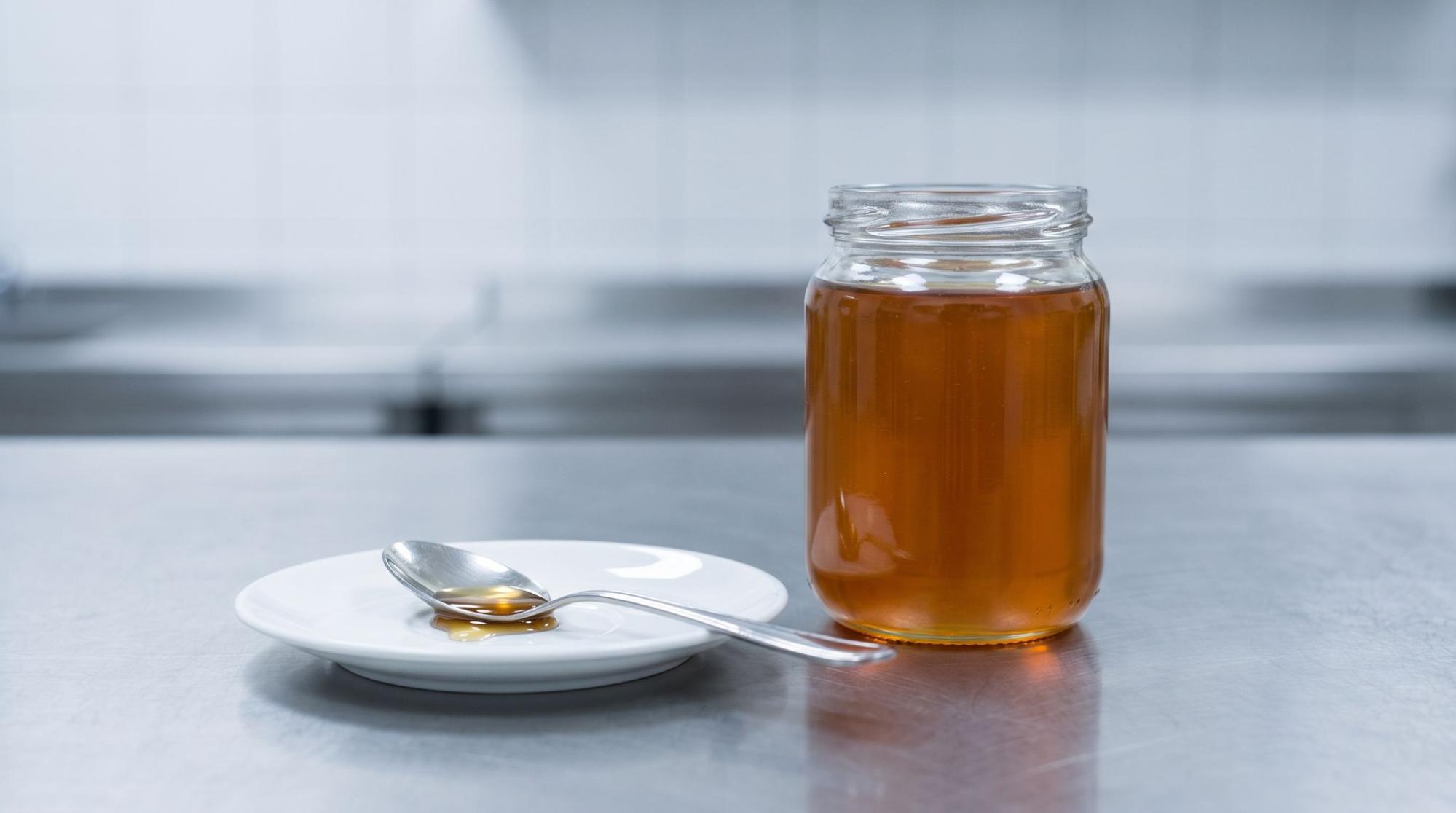  Glass jar of honey with a spoon on a kitchen countertop
