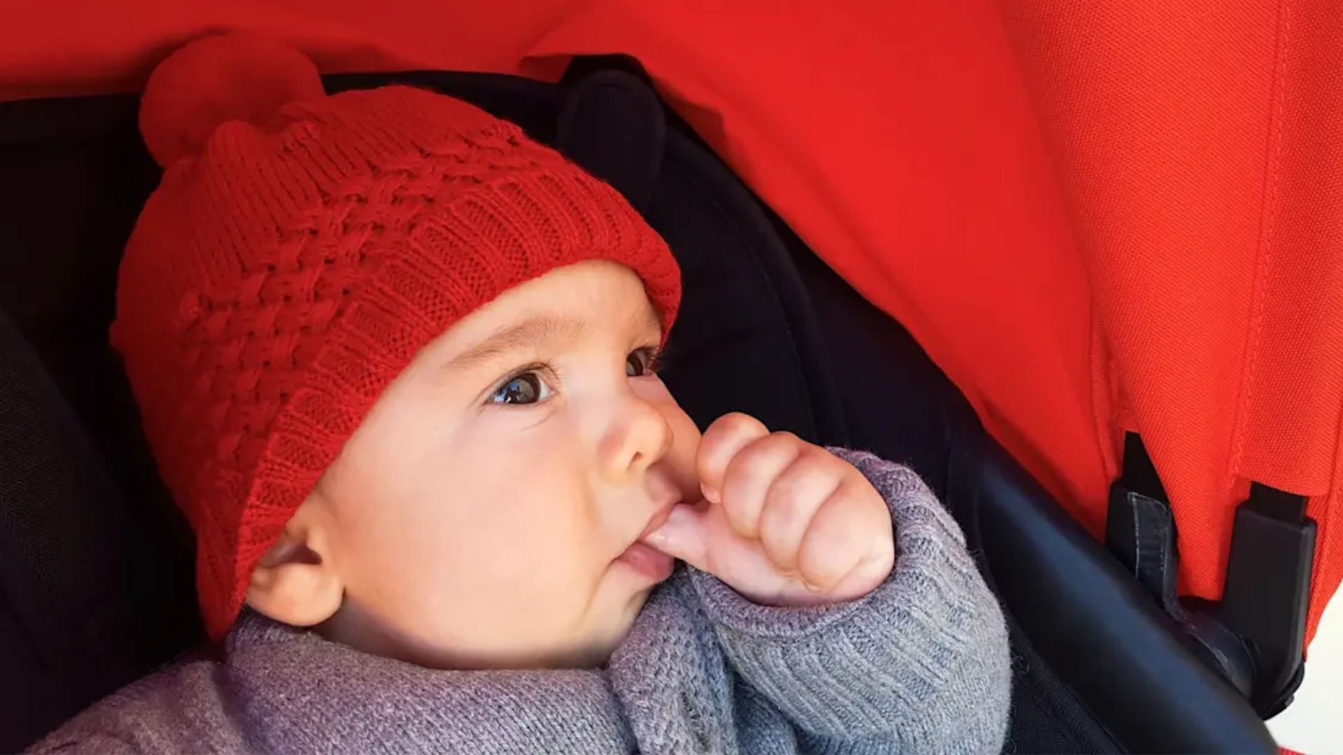 Infant lying on a play mat with thumb in mouth, looking calm and alert